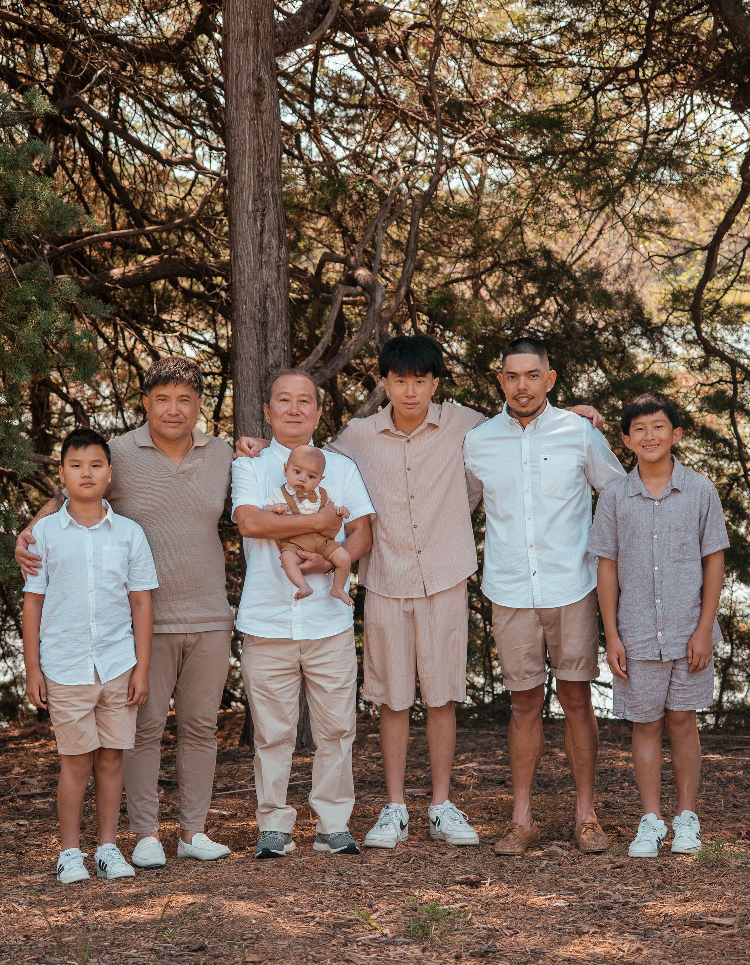 Line of children in coordinated beige and white outfits standing together under pine trees.