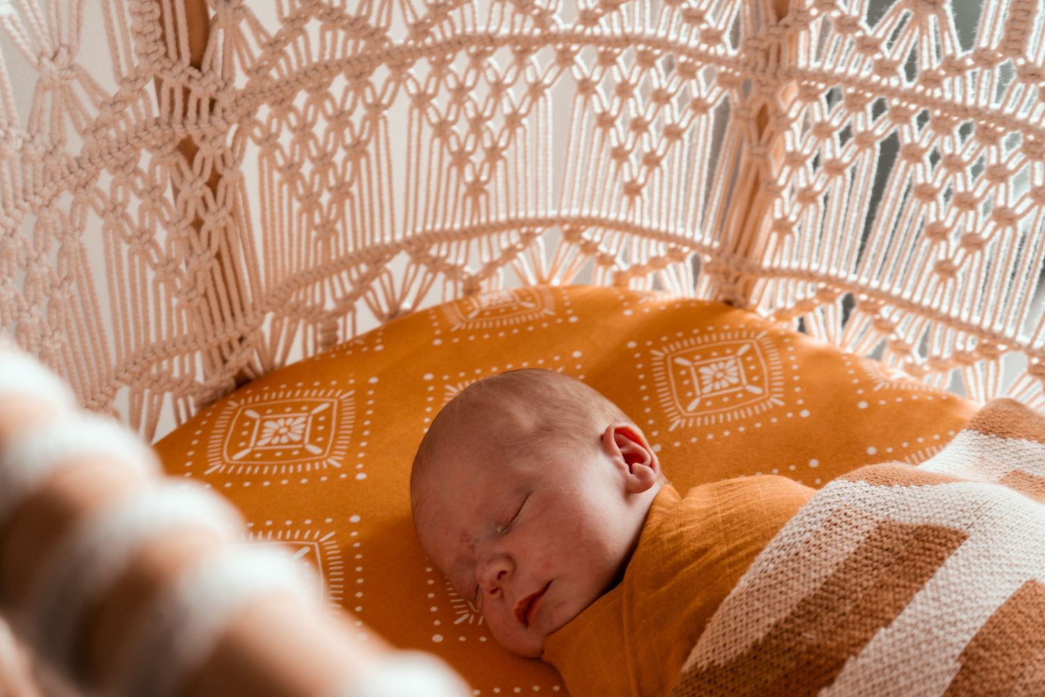 Sleeping newborn baby on orange fabric with decorative lace pattern overhead.