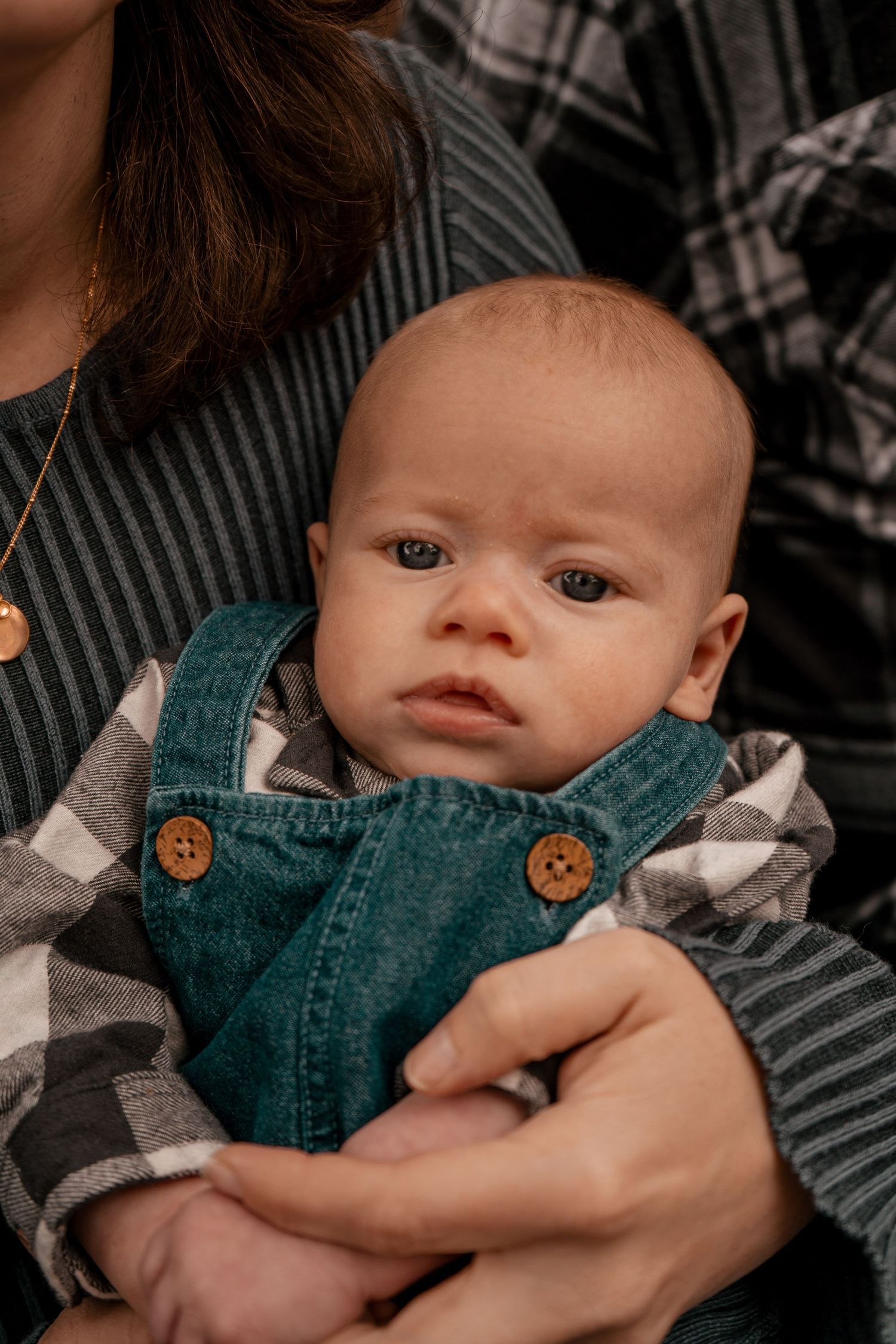 Close-up photos of a baby wearing a teal corduroy outfit with wooden buttons against a plaid blanket background.