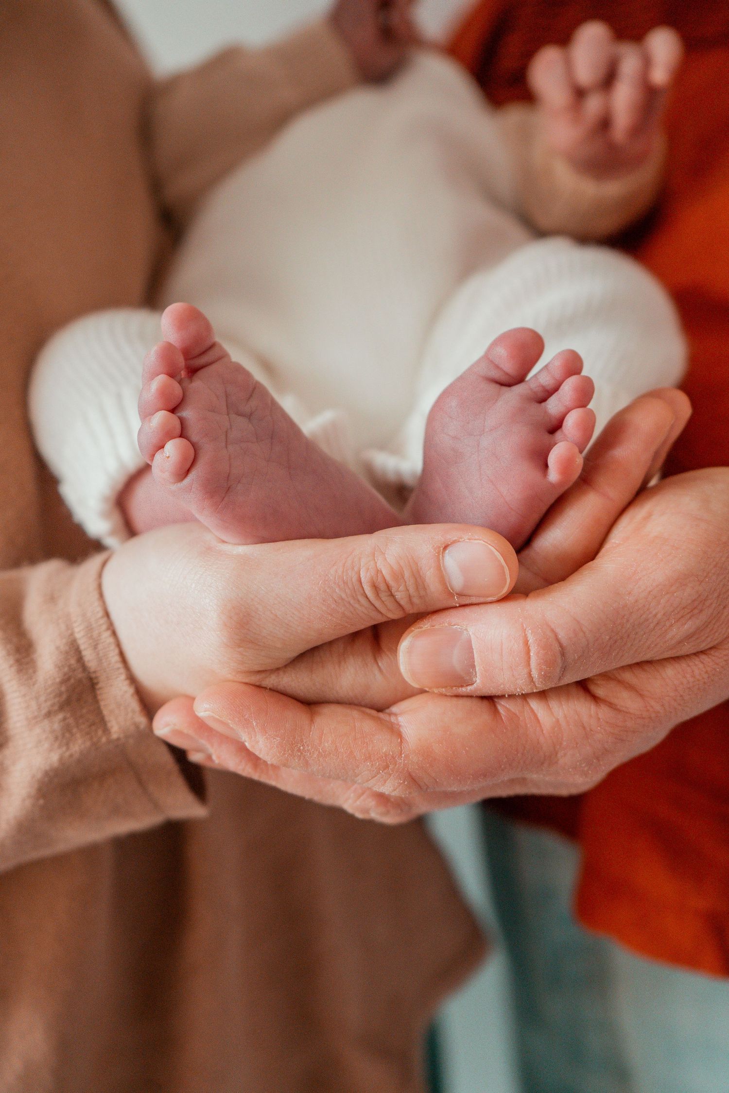 Gentle hands holding and massaging tiny newborn baby feet in a warm, nurturing setting.