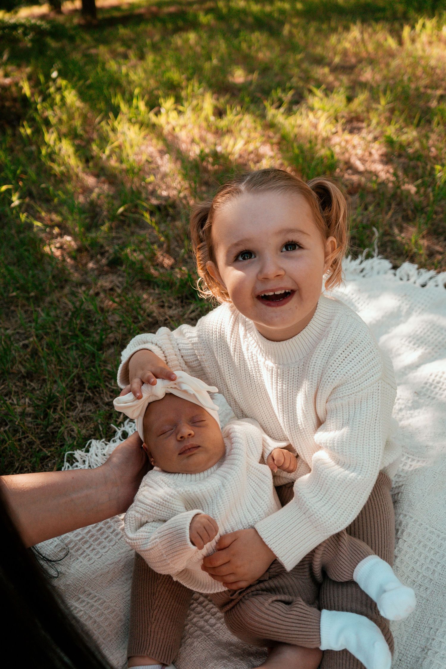 A heartwarming outdoor scene of siblings in white sweaters sharing a joyful moment on a blanket.