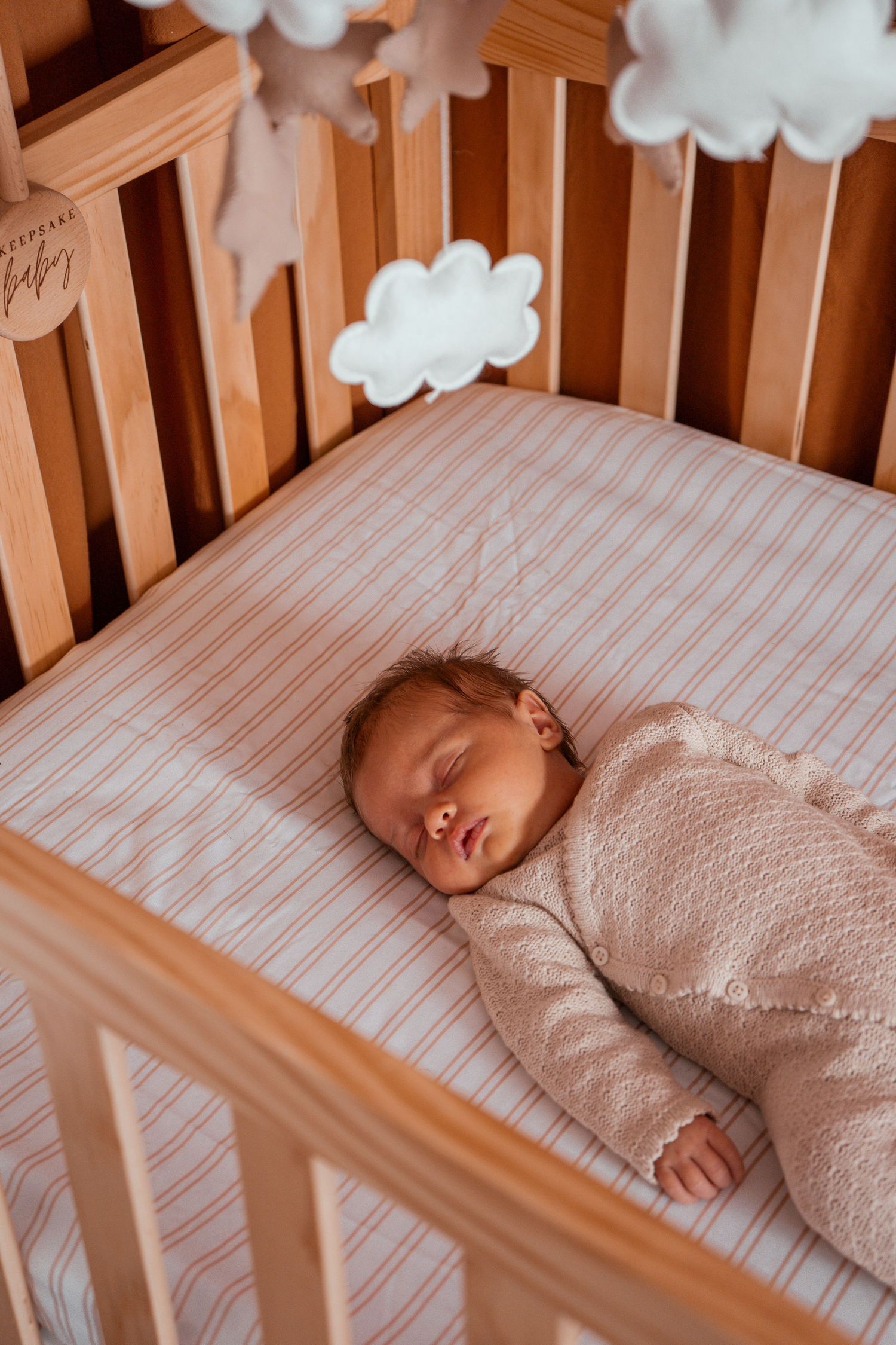 A peaceful nursery scene with a wooden crib, striped bedding, and decorative white cloud accents on the wall.