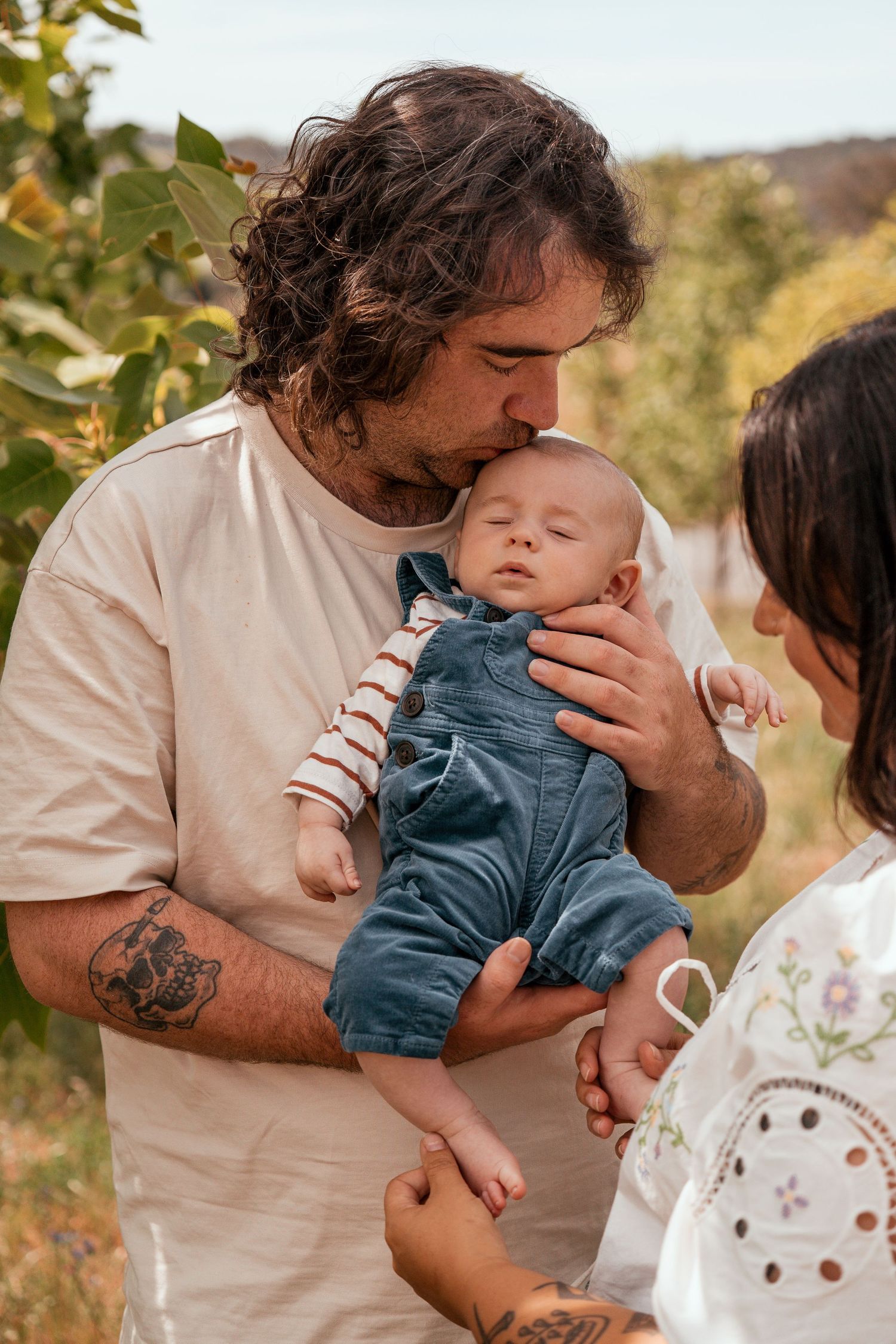 A parent in a white t-shirt shares tender moments with a small child outdoors against a natural backdrop.