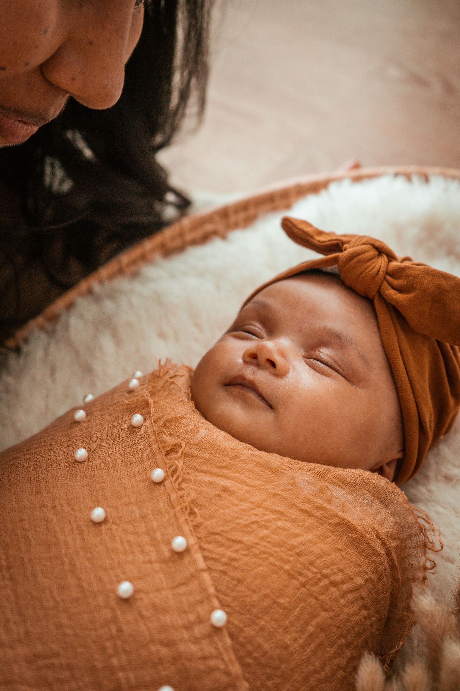 Sleeping baby wearing brown knit clothing lies peacefully on soft white blanket.