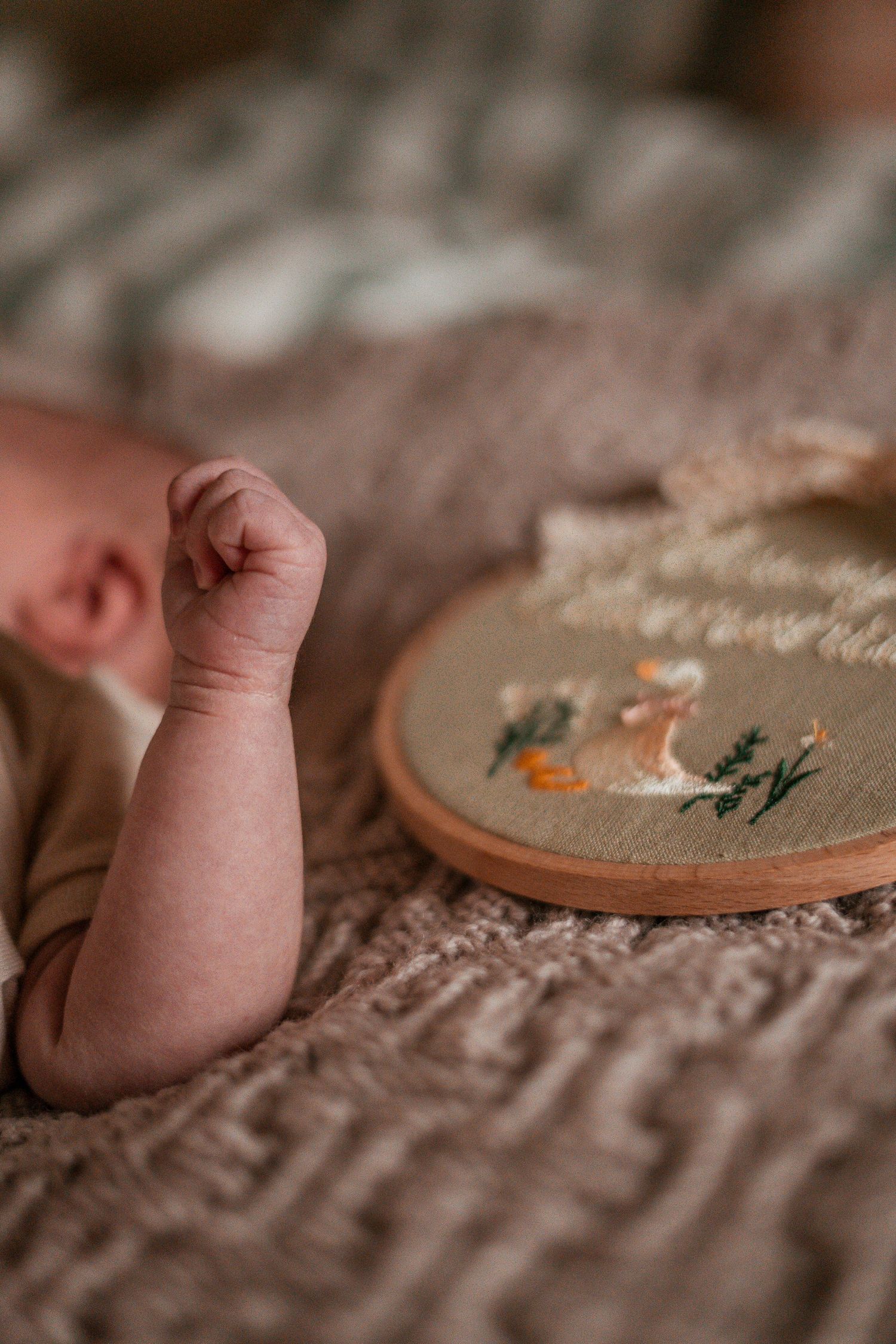 A series of close-up shots showing tiny baby feet next to embroidery hoops on a textured beige fabric background.