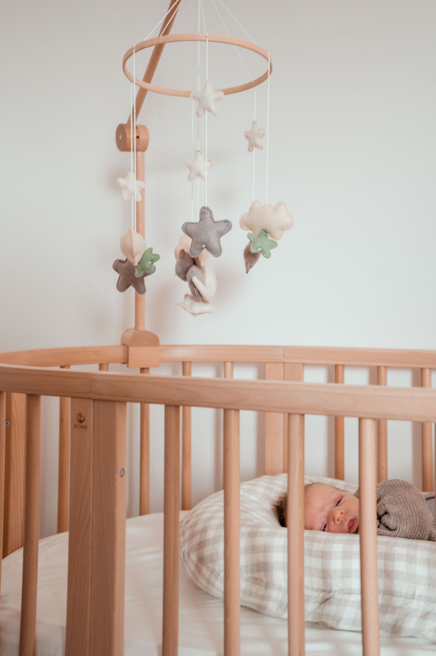 A wooden crib with a mobile featuring soft plush stars and flowers hanging above it.