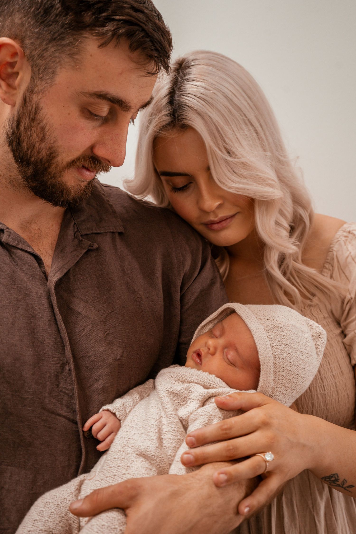 A tender family moment as parents cradle their sleeping newborn wrapped in white knit blankets.