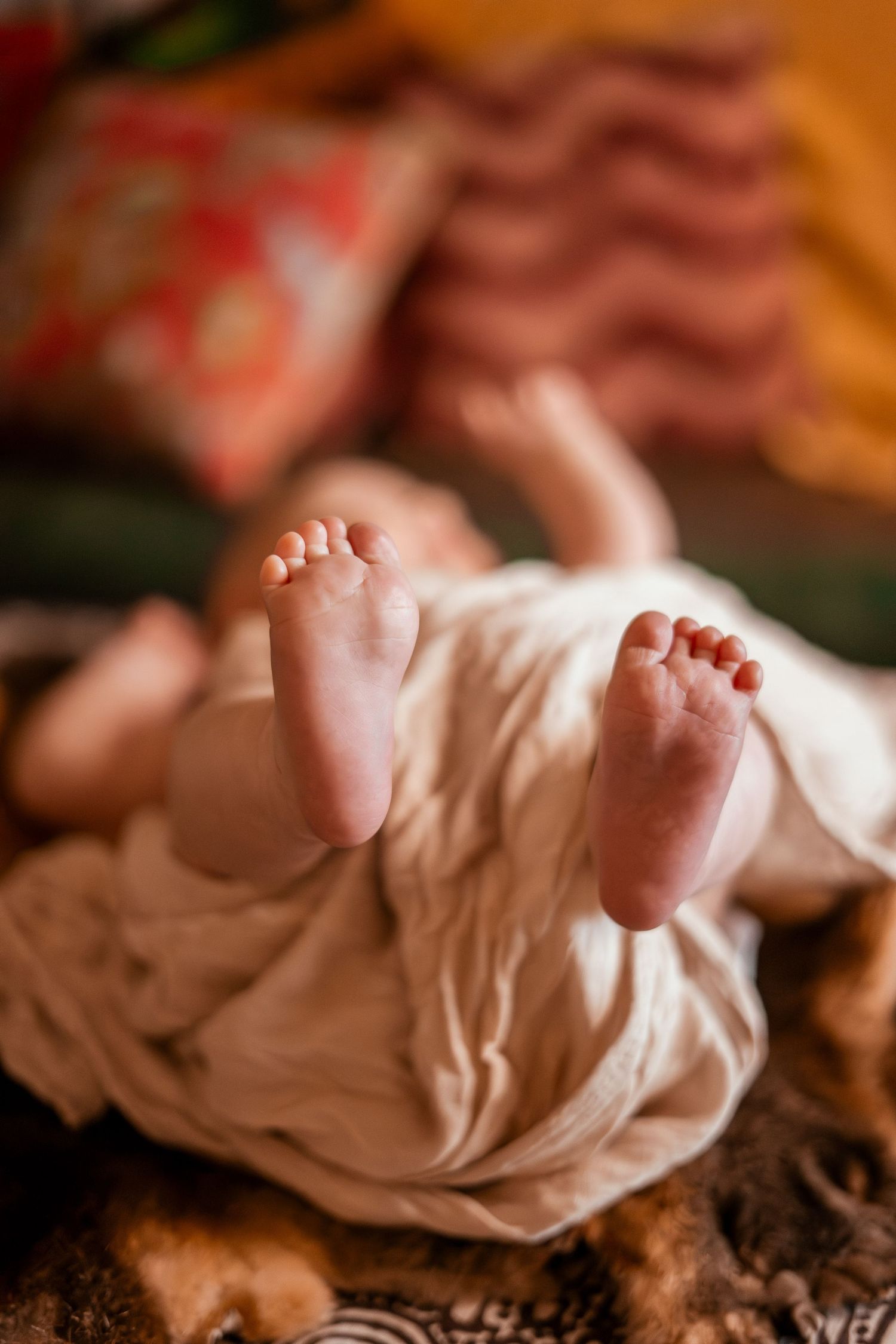 Close-up sequence showing tiny baby feet emerging from soft white fabric in warm lighting.