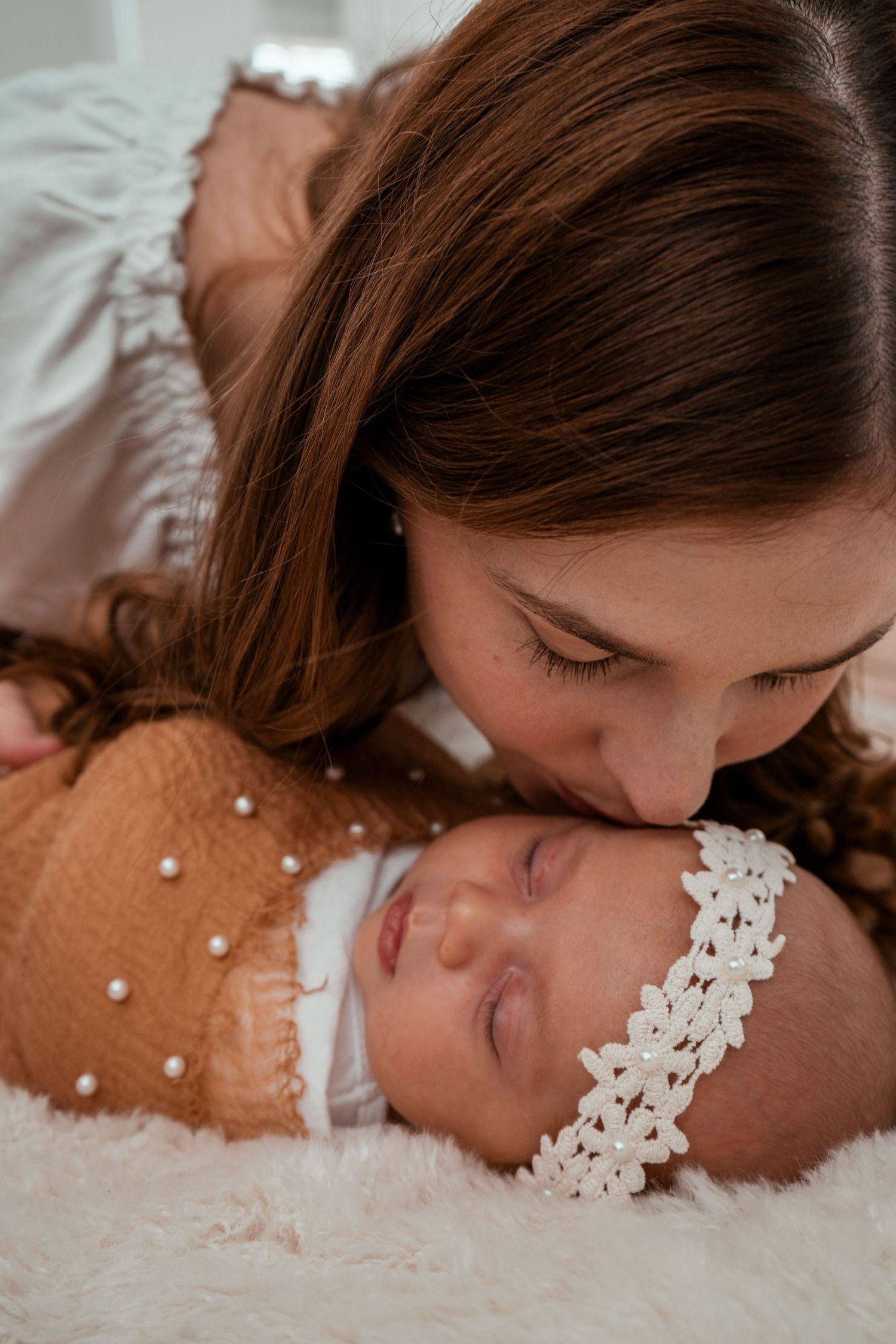 A tender moment captured of a mother and newborn baby lying together on white fur bedding.