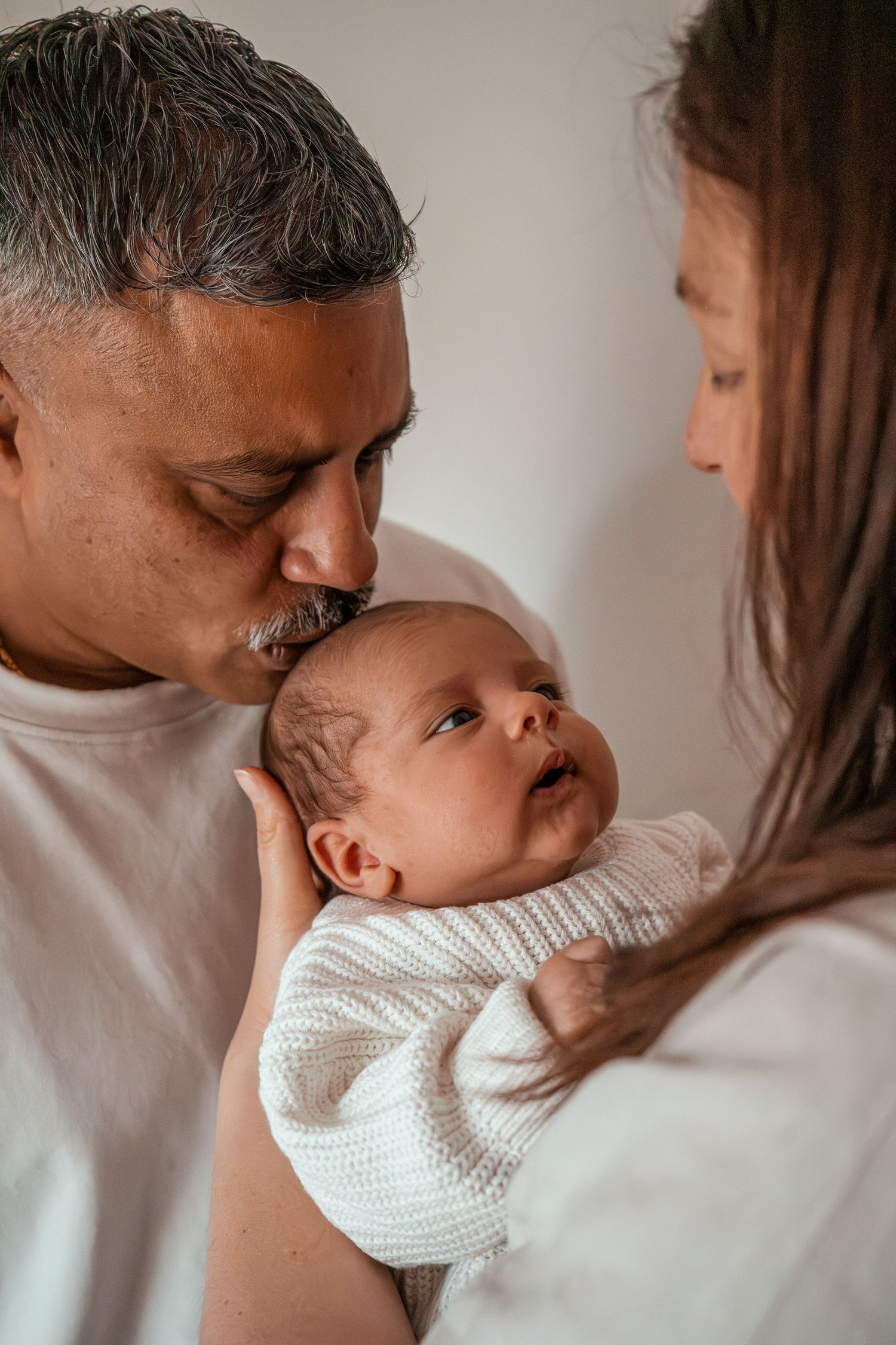 A tender moment captured in a series of intimate photos showing gentle interaction with a newborn baby in white knitwear.