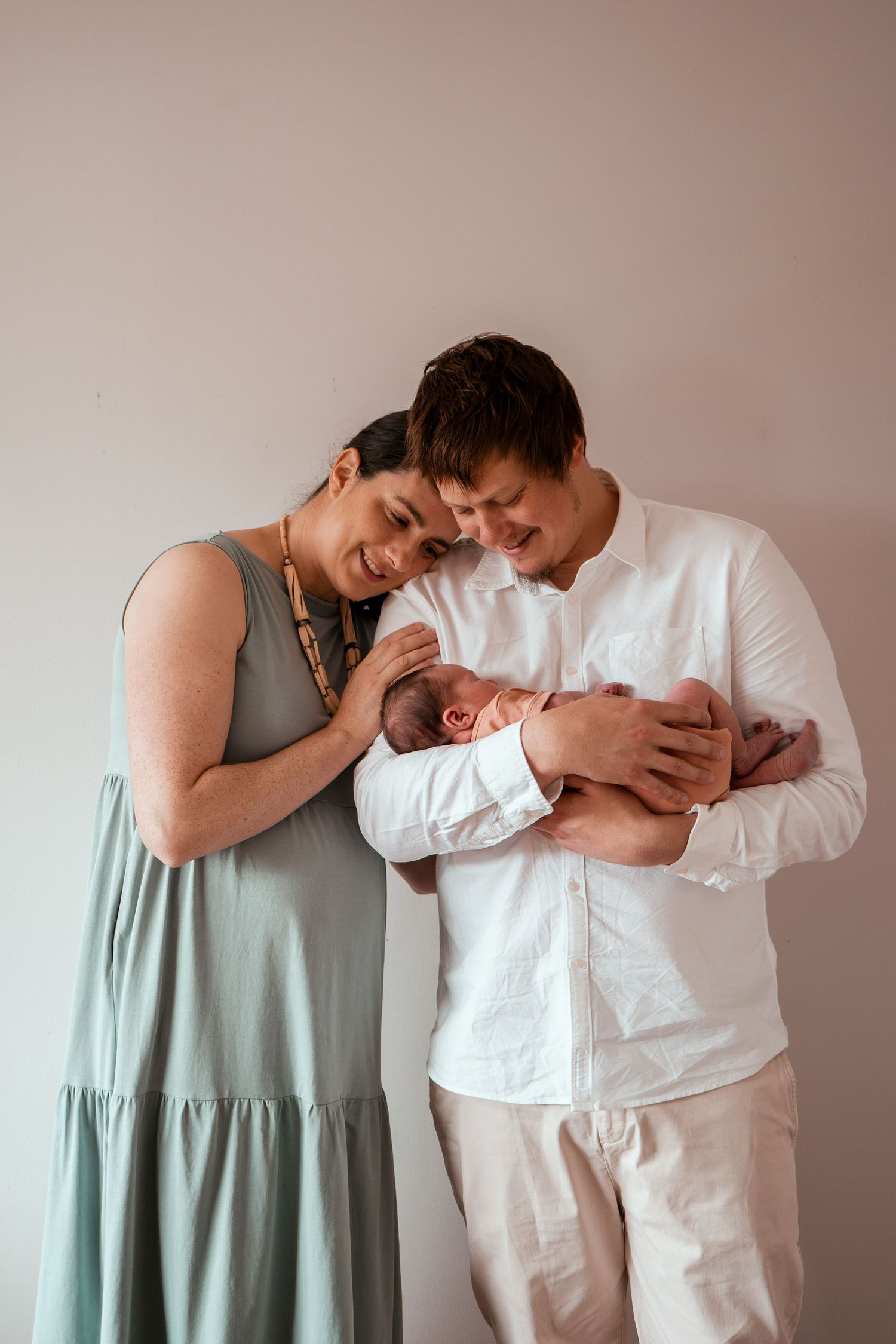 A series of intimate family portraits showing tender moments with a newborn baby against a neutral background.