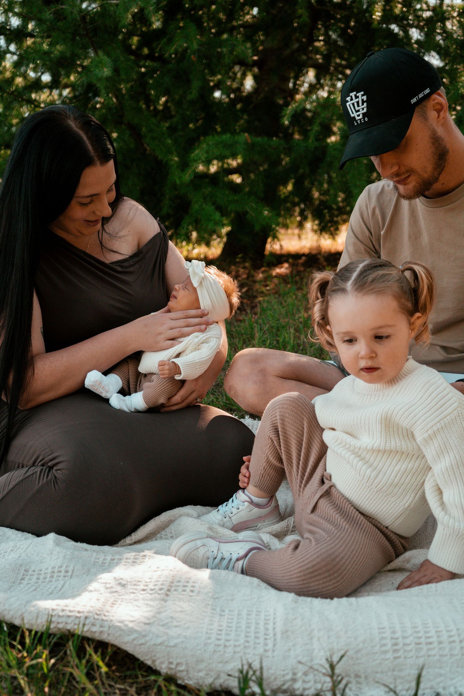 A family relaxing on a white blanket outdoors during a sunny afternoon photo session.