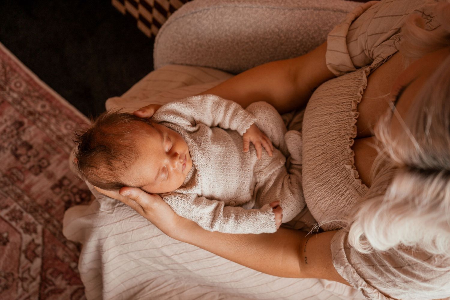 A sleeping baby in white swaddle blanket rests peacefully on soft bedding in natural light.