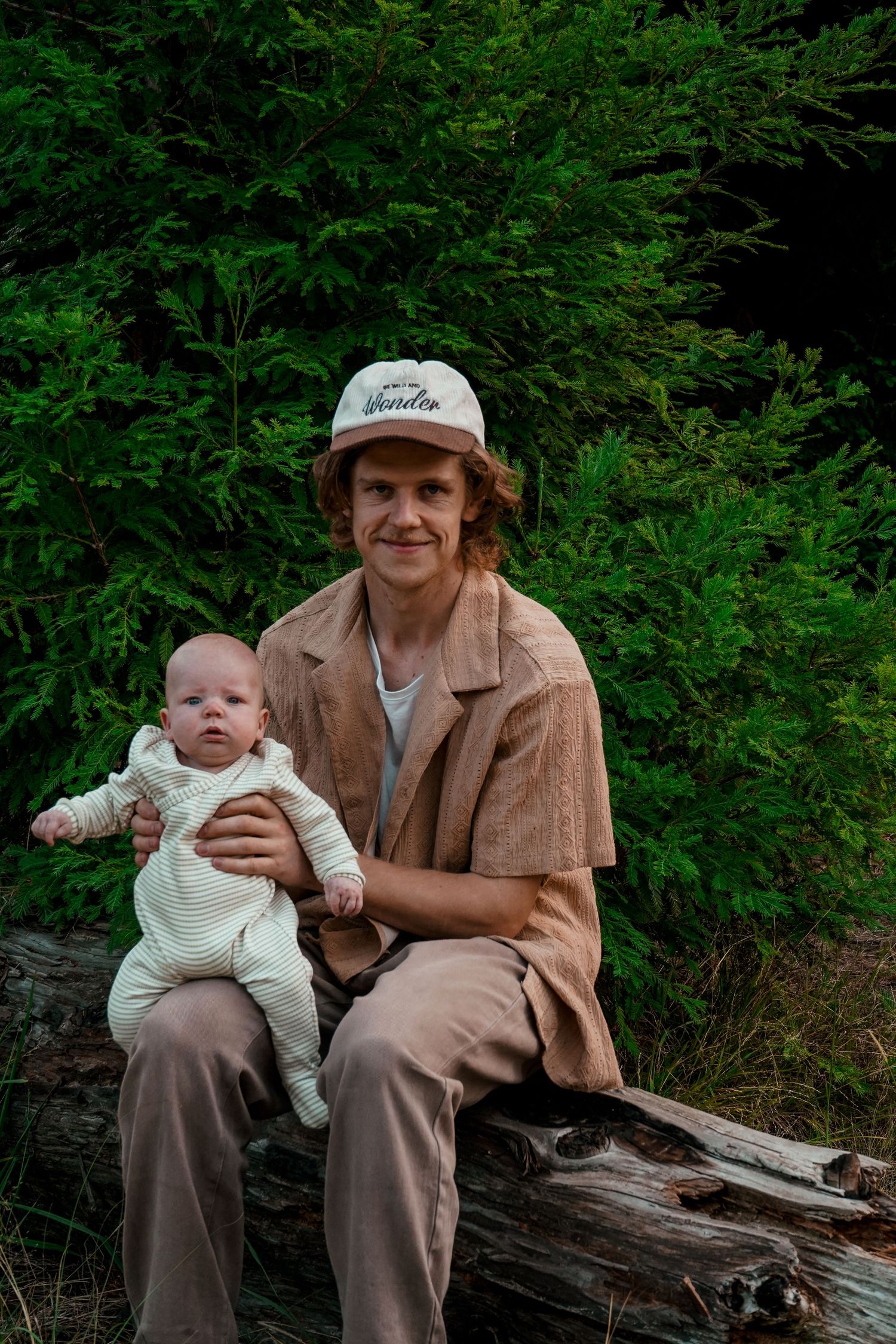 Parent and baby sitting on log against green forest background.