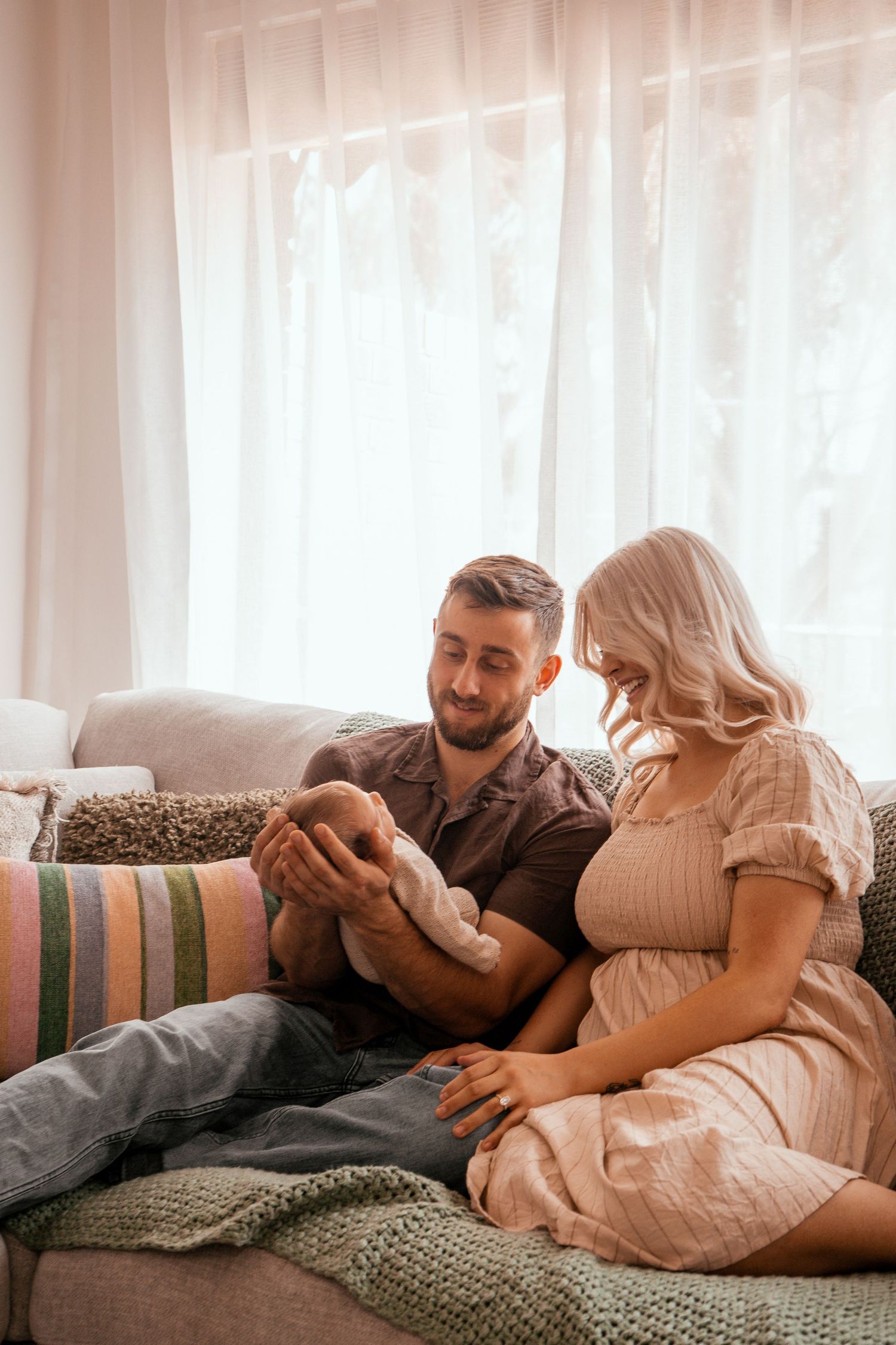 Intimate couple lounging on striped couch in bright sunlit room with white curtains and knit blanket.