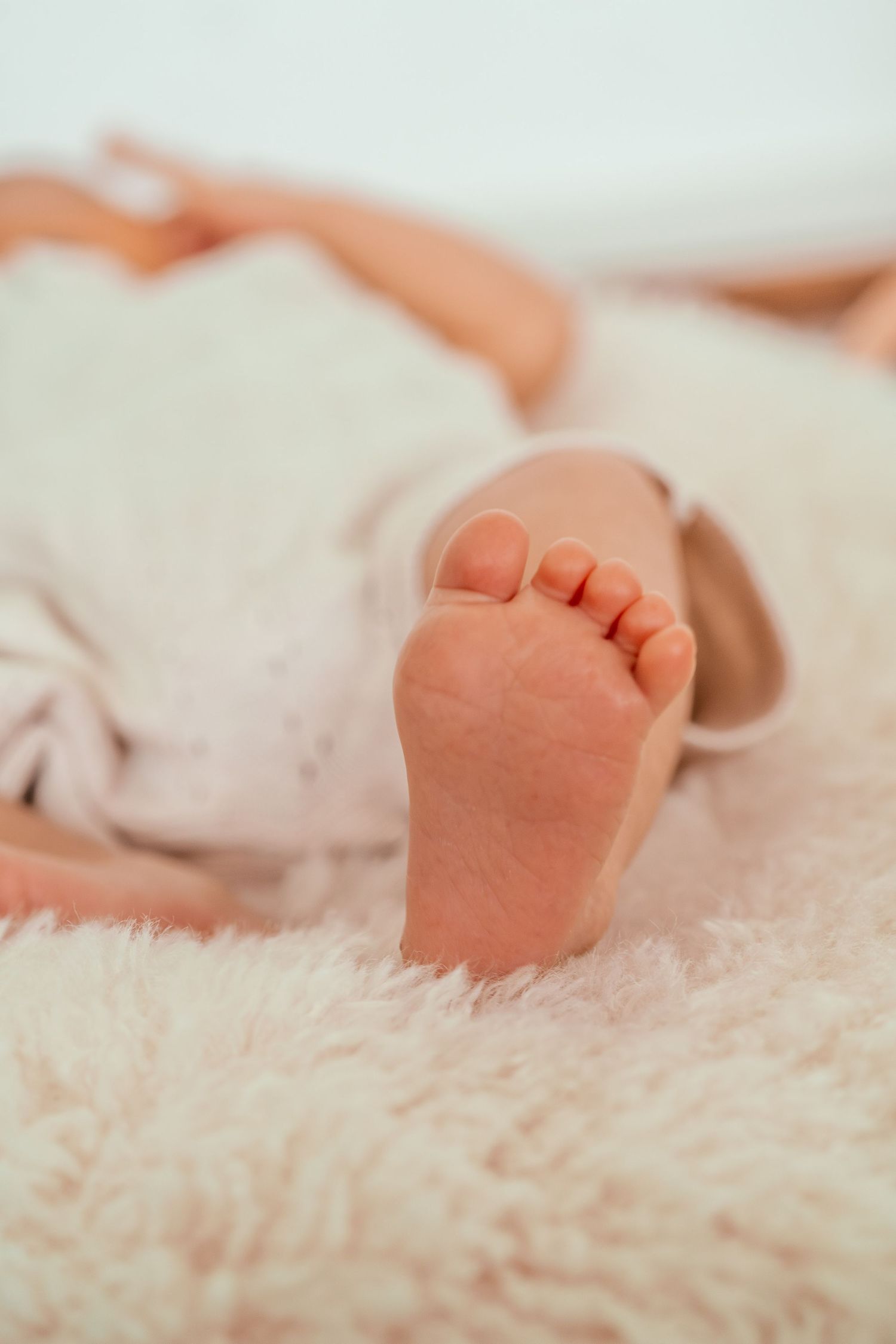 Tiny baby feet resting on soft white fluffy blanket in gentle natural lighting.