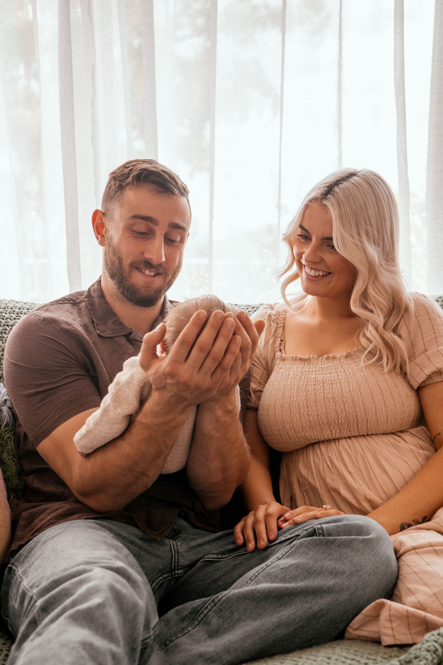 A couple shares a joyful moment together on their living room couch while holding their newborn.