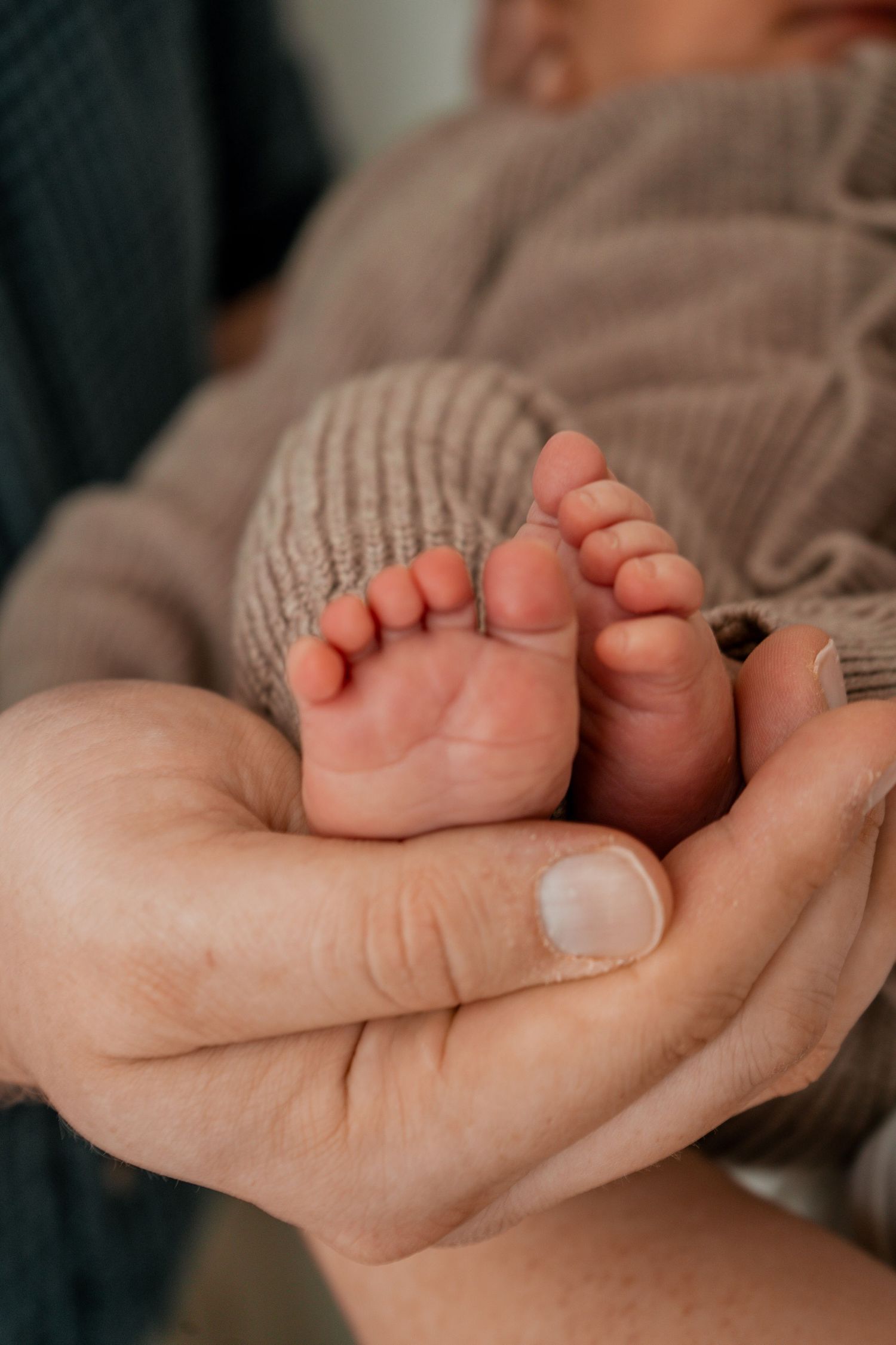 Gentle hands cradling tiny newborn feet wrapped in soft brown knitted fabric.