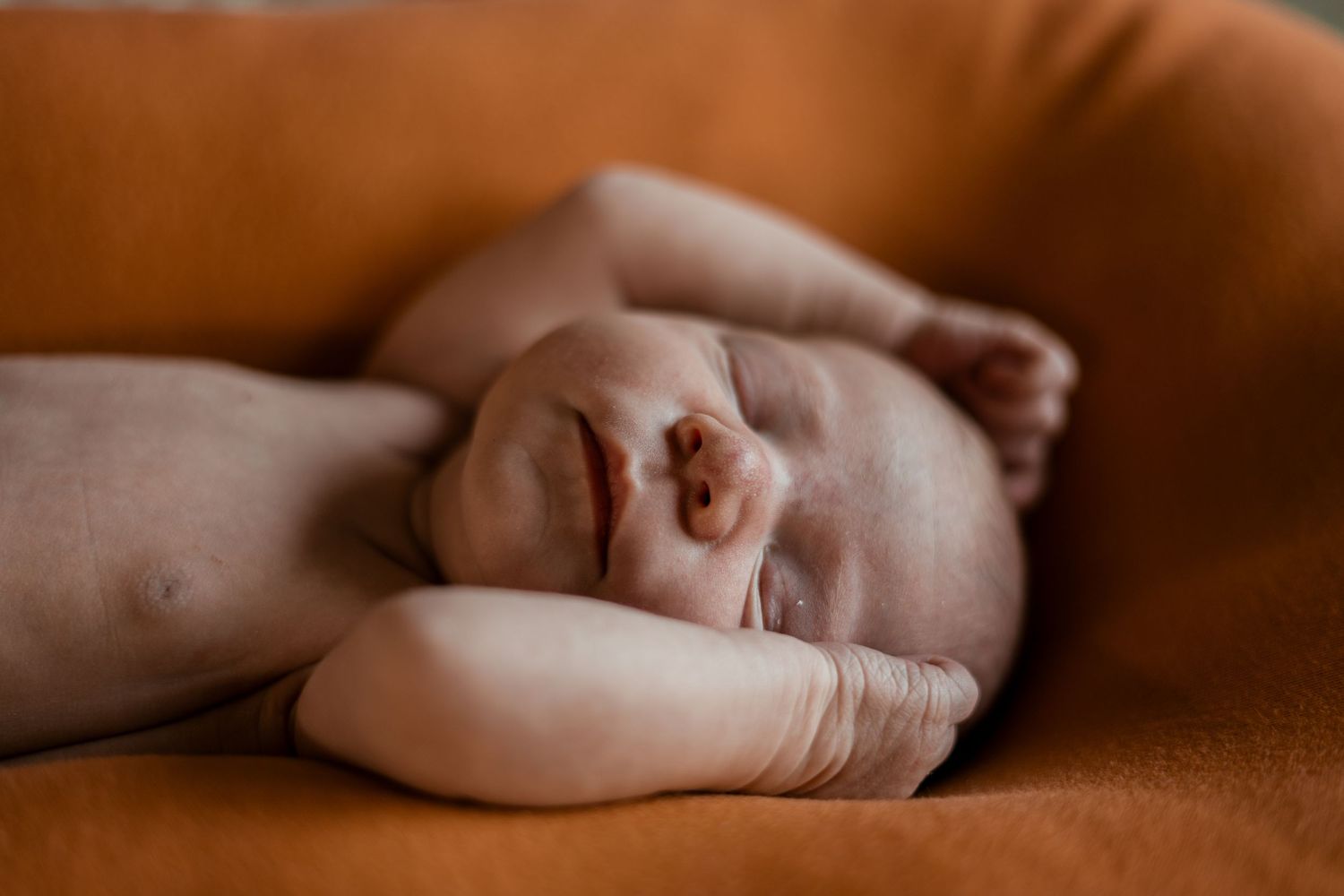 Close-up of sleeping baby's peaceful face resting on orange cushion.