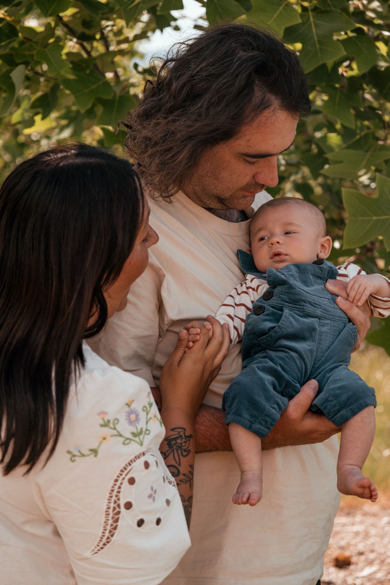 A tender moment captured between parents and their baby outdoors against a backdrop of green foliage.