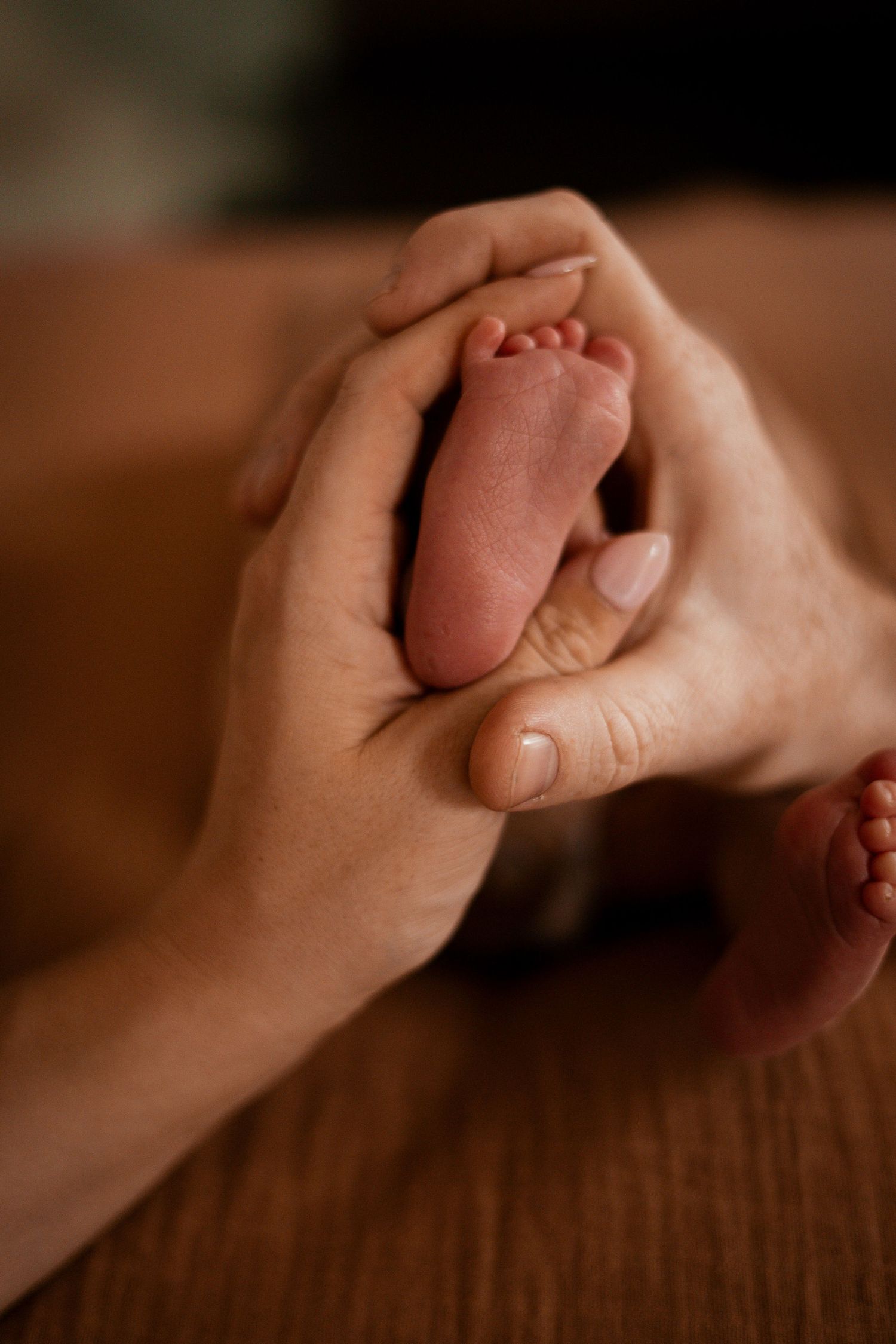 Close-up sequence of hands holding and gently caressing a tiny newborn baby hand against a wooden surface.