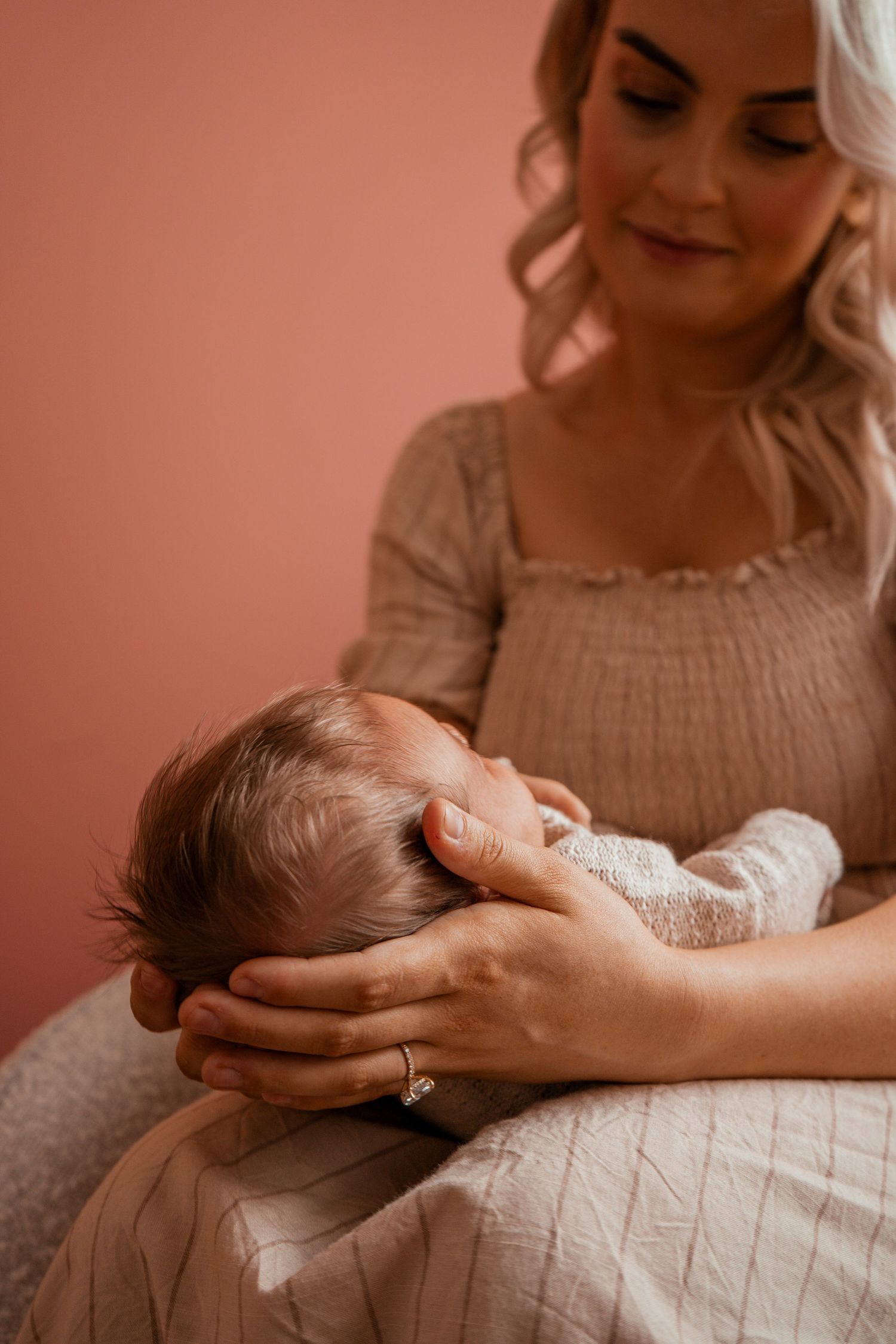 A tender moment in a nursery as a caregiver cradles a sleeping infant against soft pink walls.