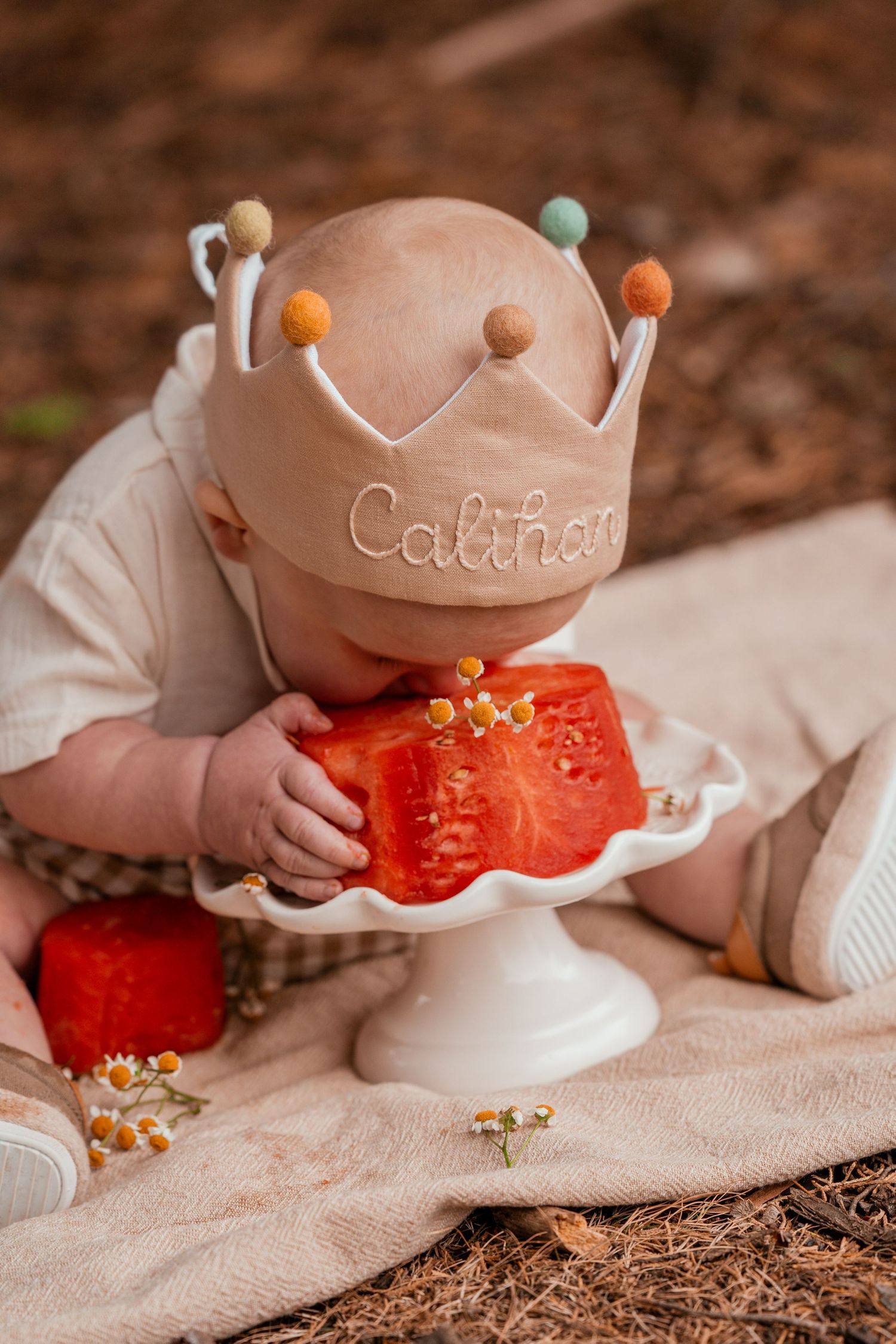 Close-up sequence showing a baby in a white hat reaching for and playing with a red watermelon slice on a beige blanket.