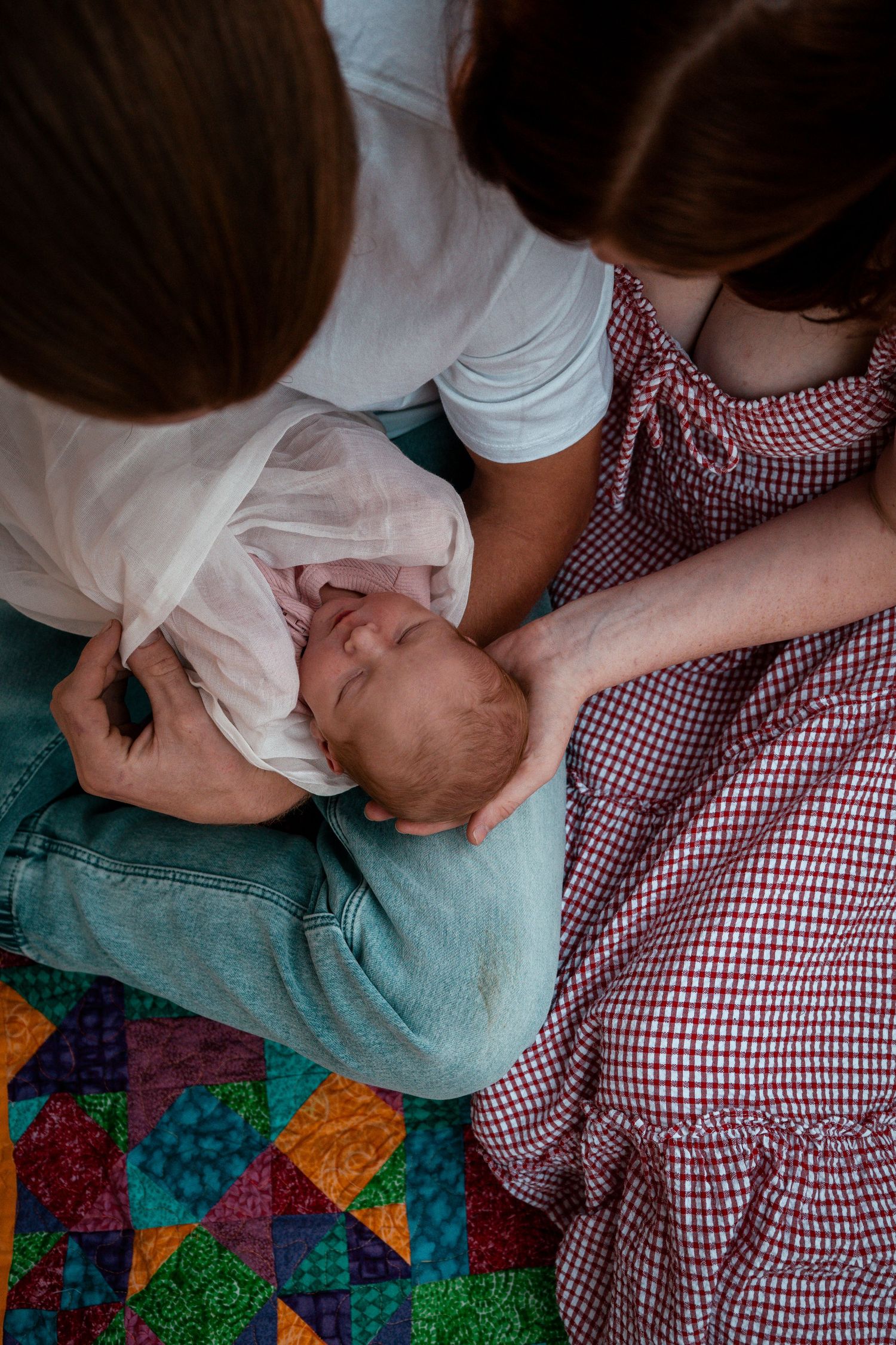Family gathering around baby on colorful patchwork quilt.