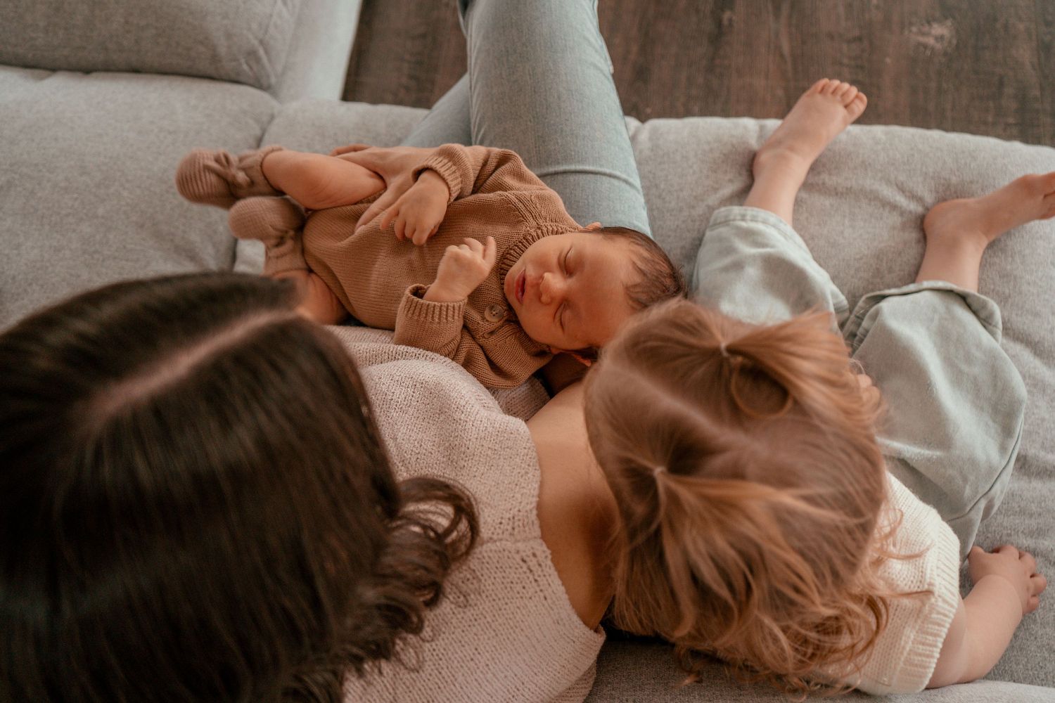 Siblings lying together on light gray couch in casual clothing.