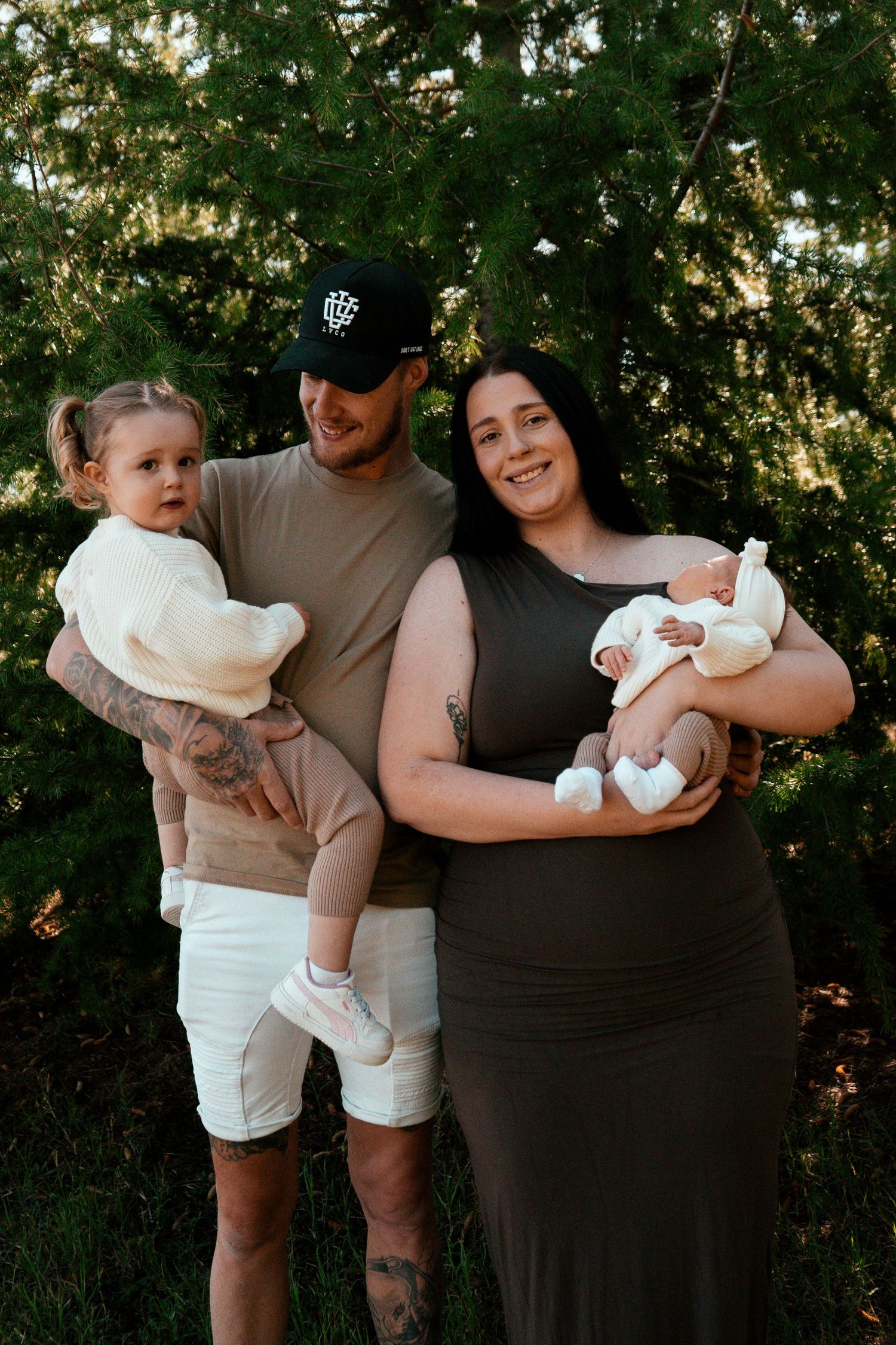 Casual outdoor family portrait with toddler and newborn on sunny day.