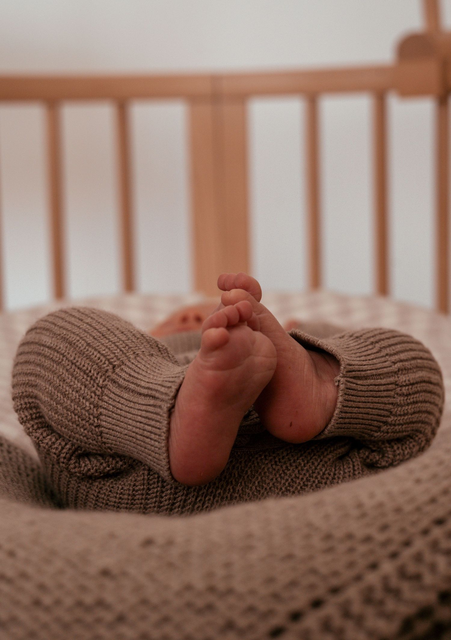Tiny newborn baby feet wearing cozy brown knitted booties while resting on textured fabric.