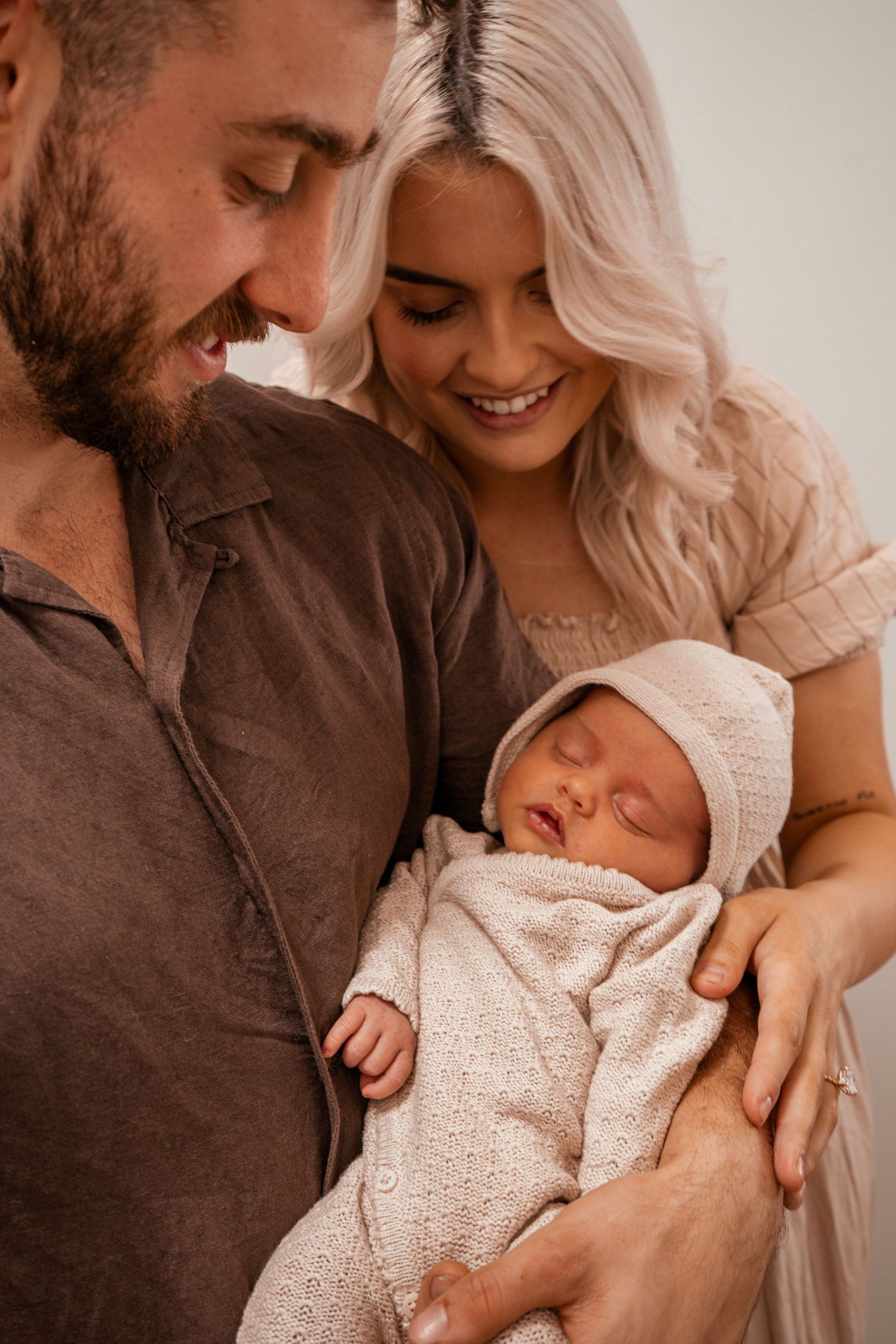 A tender family moment as parents hold their newborn baby wrapped in a soft cream-colored blanket.