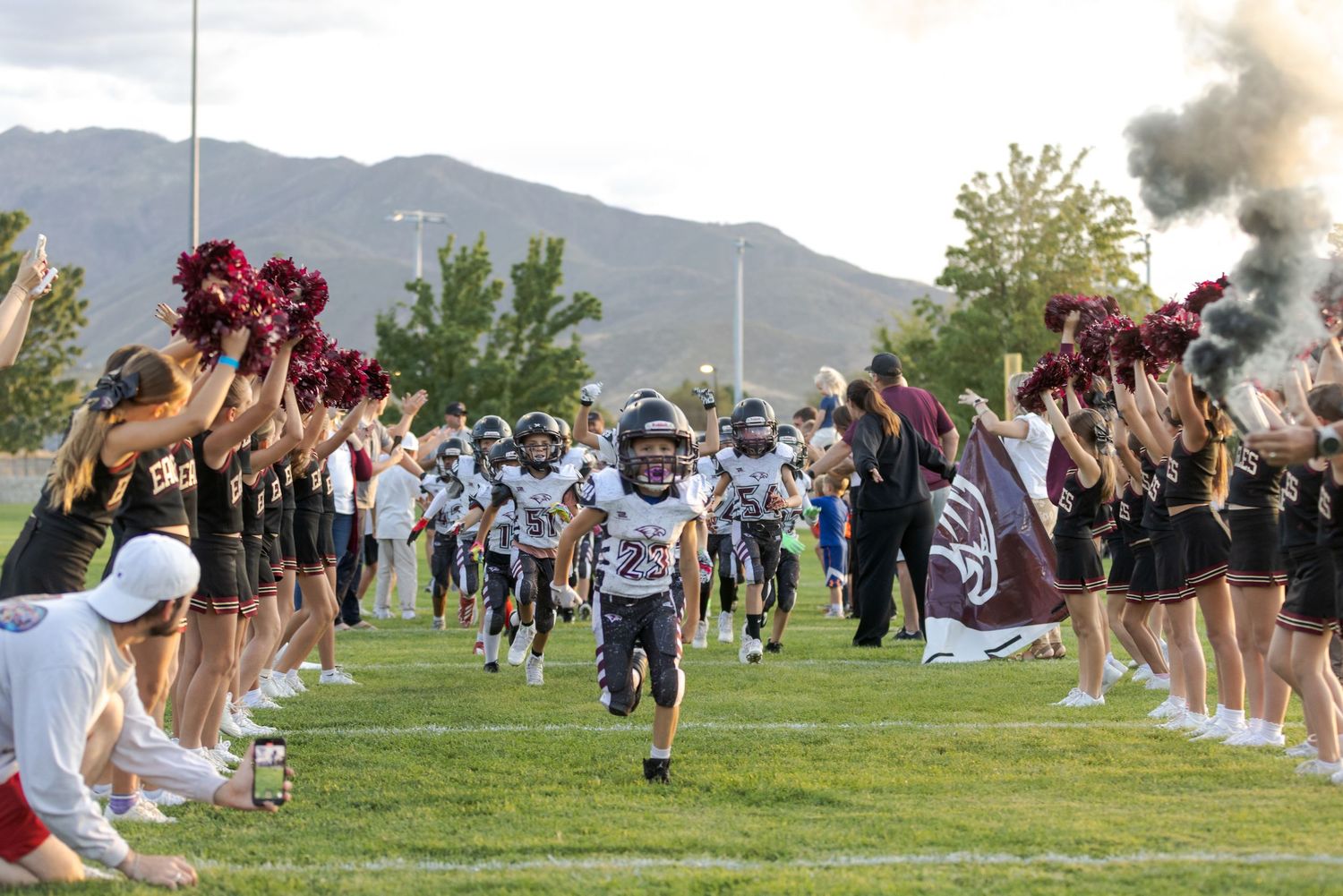 A large group of students gathers on a grassy field during an outdoor school event with mountains in the background.
