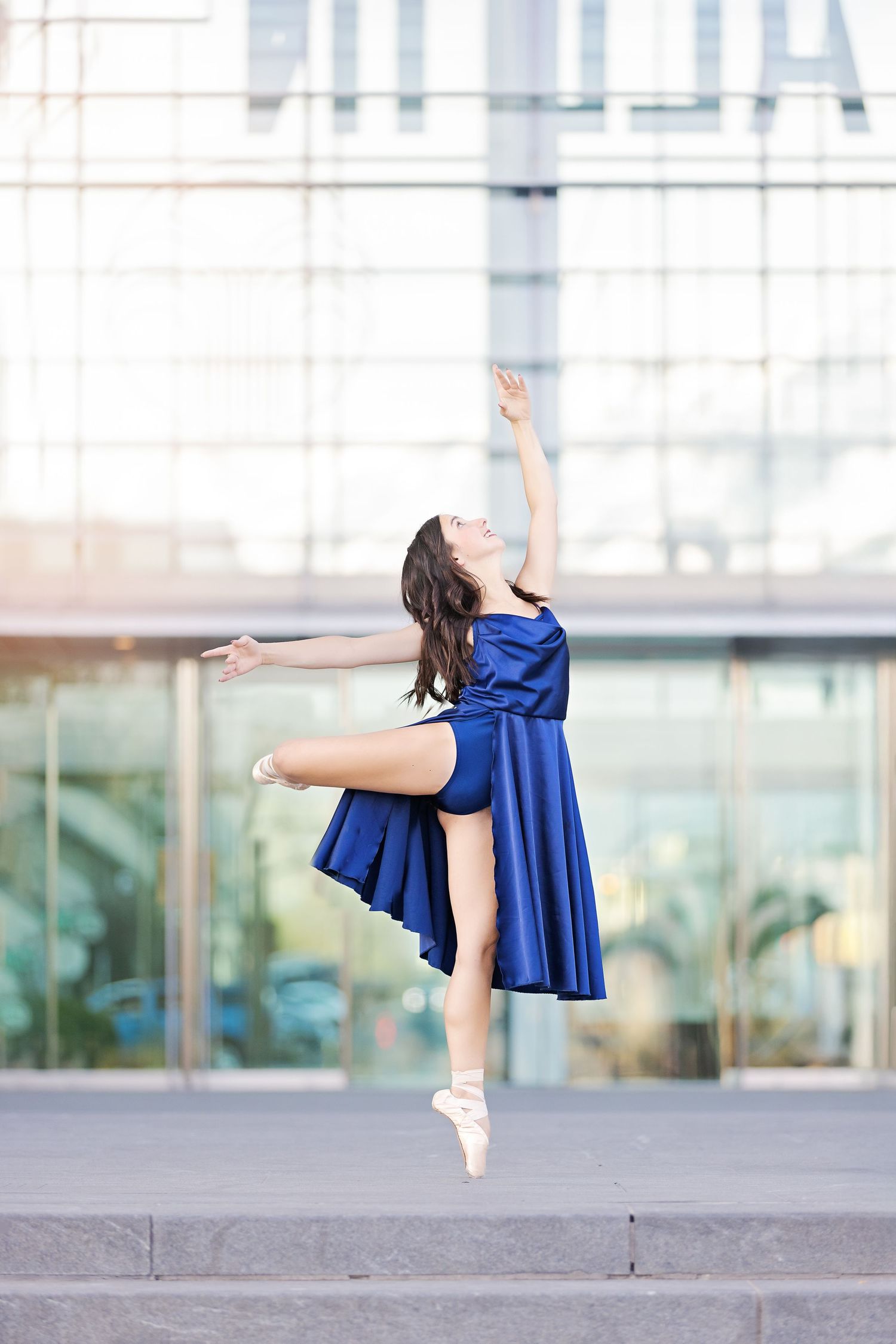 Ballerina in flowing royal blue dress performs graceful pose sequence on urban rooftop setting in natural light.