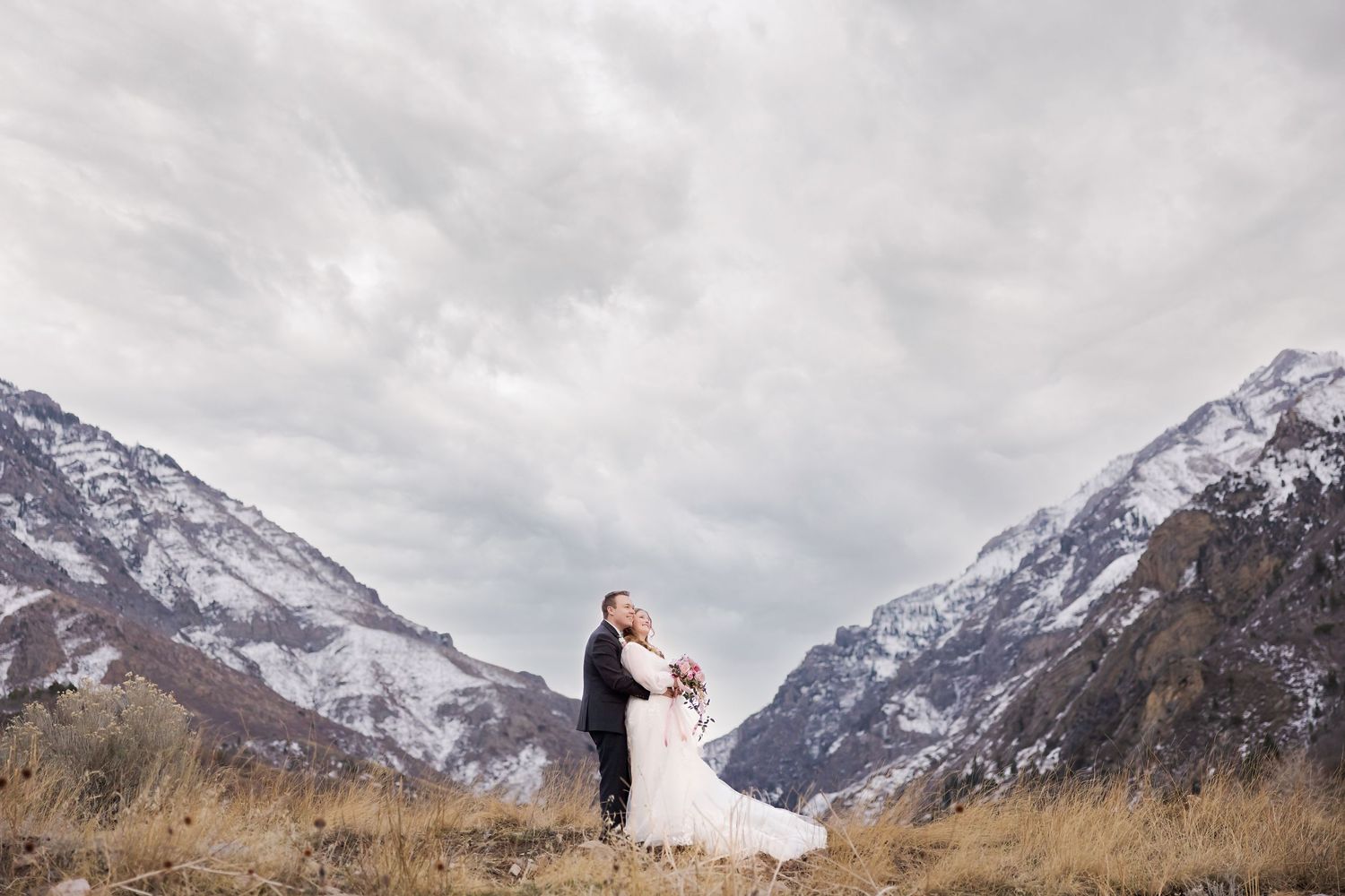 Wedding couple embracing against dramatic mountain landscape with snow-capped peaks.