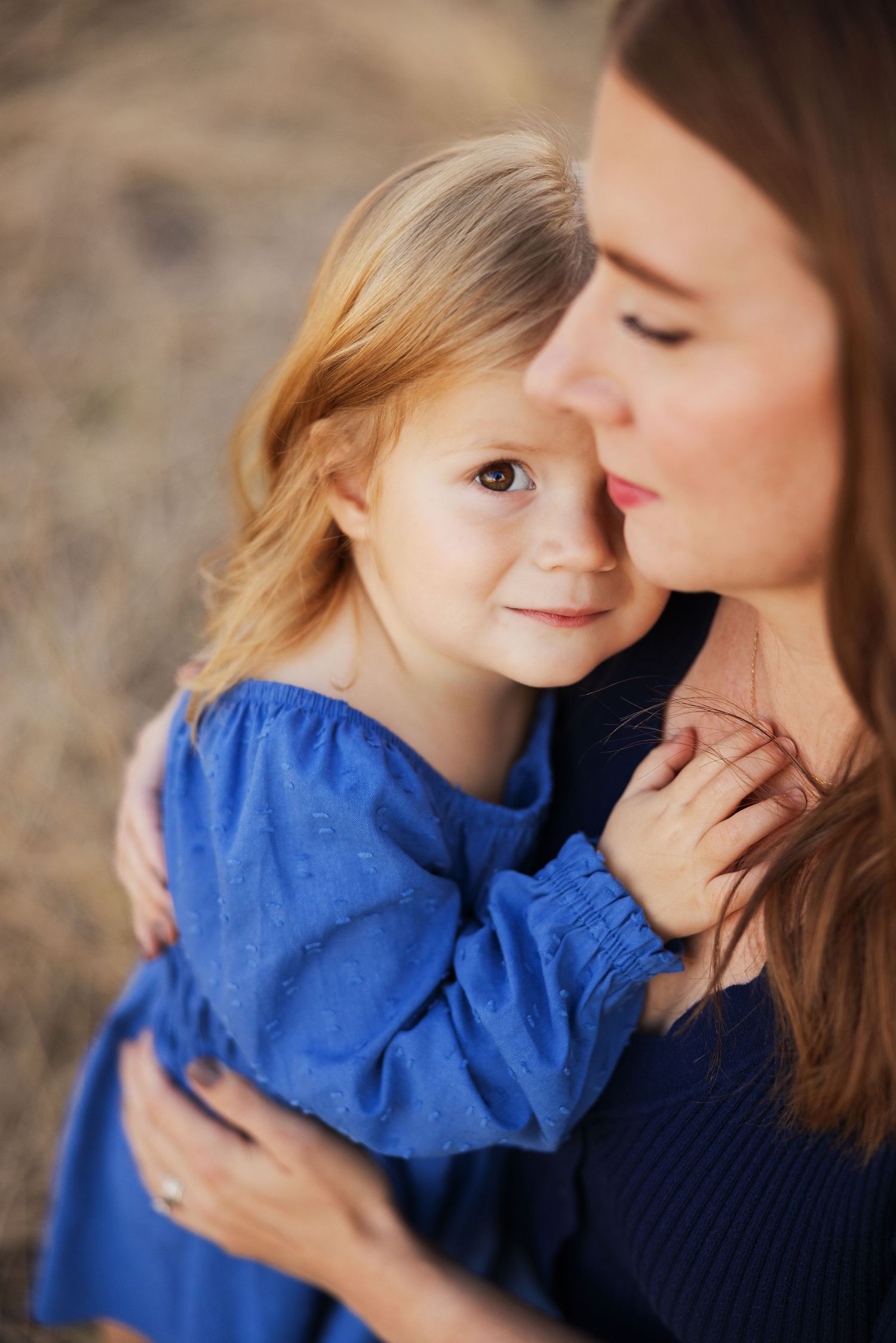 Intimate portrait of parent and child in blue dress against natural outdoor backdrop.