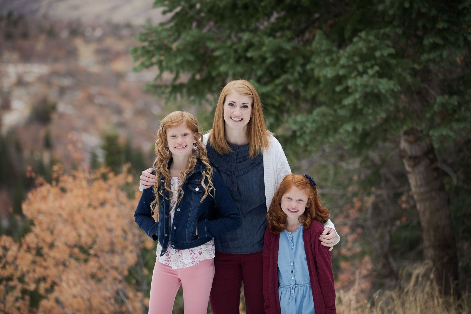 Three people pose together outdoors during fall with colorful foliage in background.