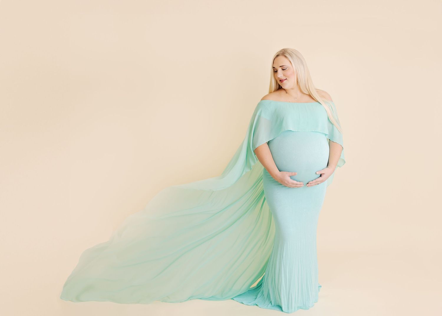 Maternity portrait of a woman in flowing mint green gown with dramatic fabric movement.