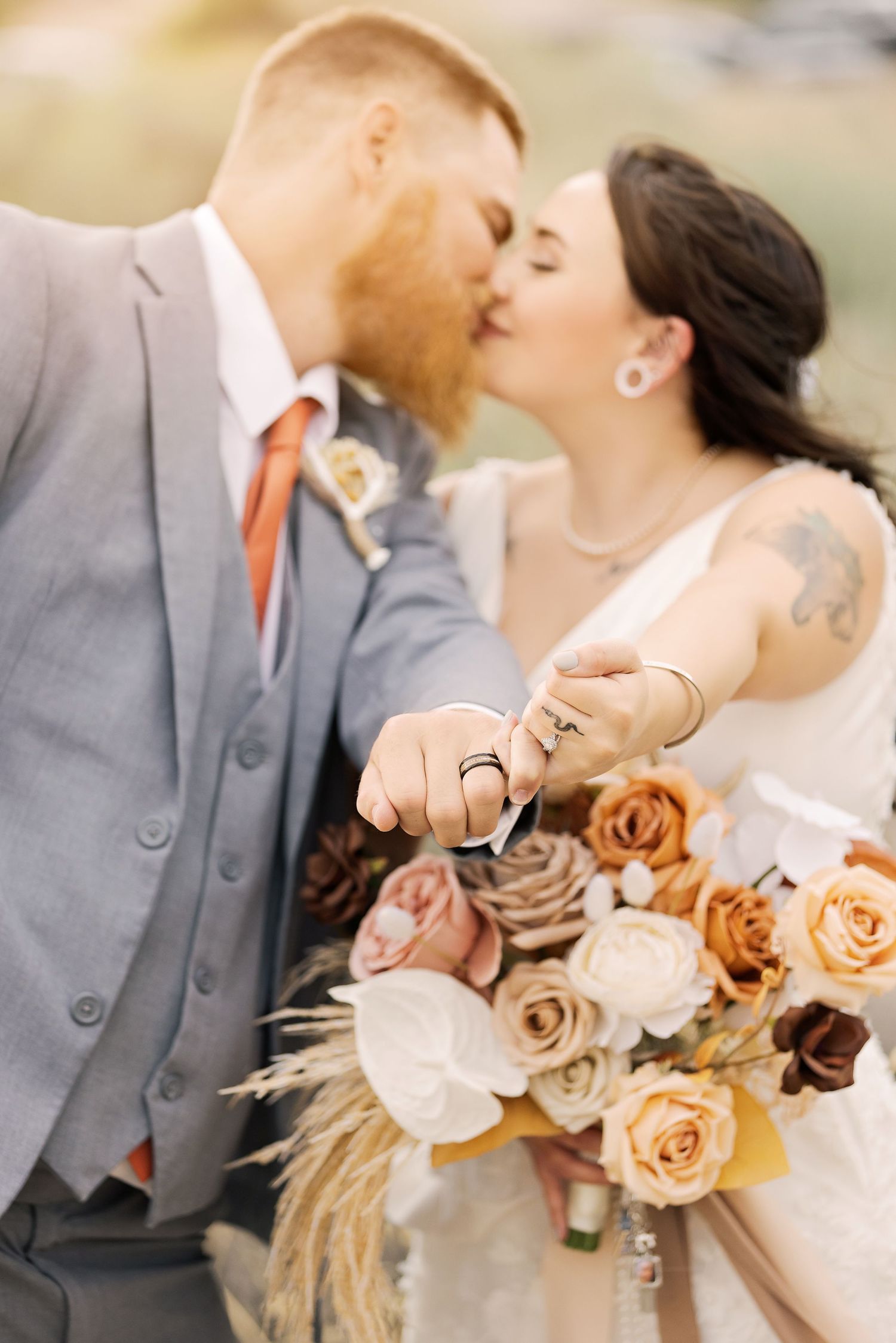 Close up of couple kissing with peach rose bouquet featuring dried pampas grass elements.
