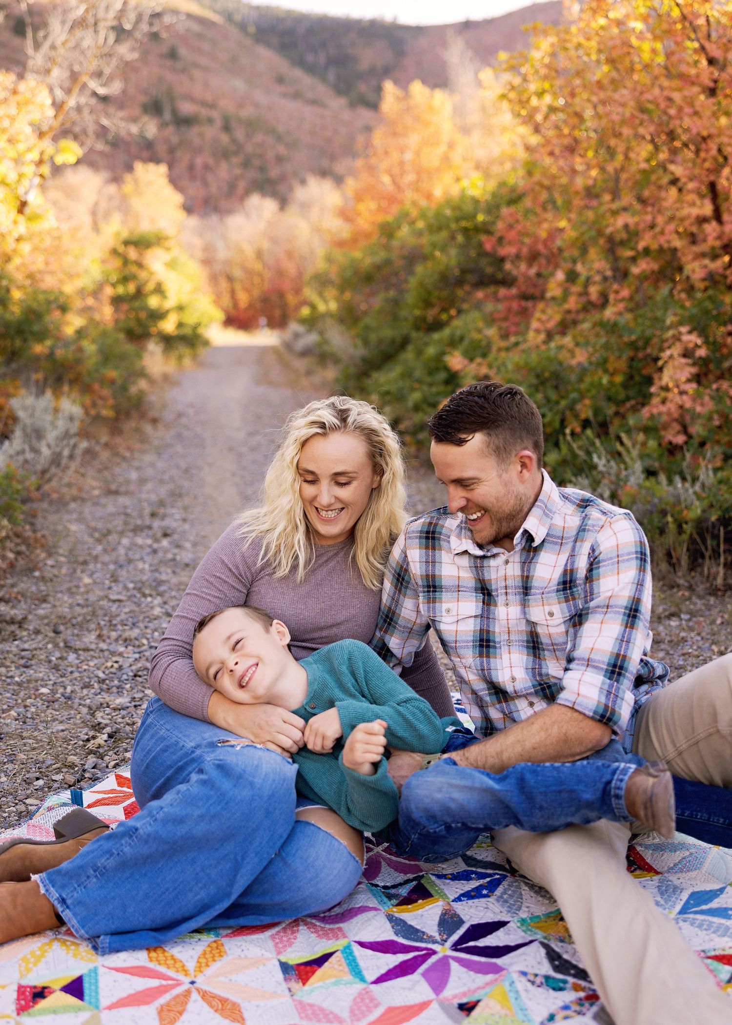 Family relaxing together on colorful blanket during autumn photoshoot on mountain trail.