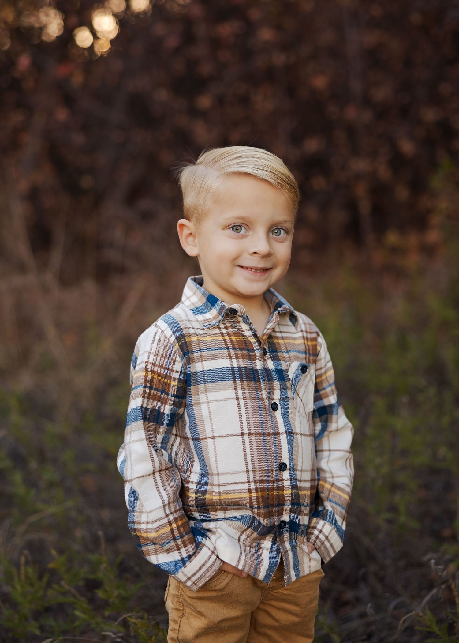 Child in plaid flannel shirt with tan pants stands outdoors.