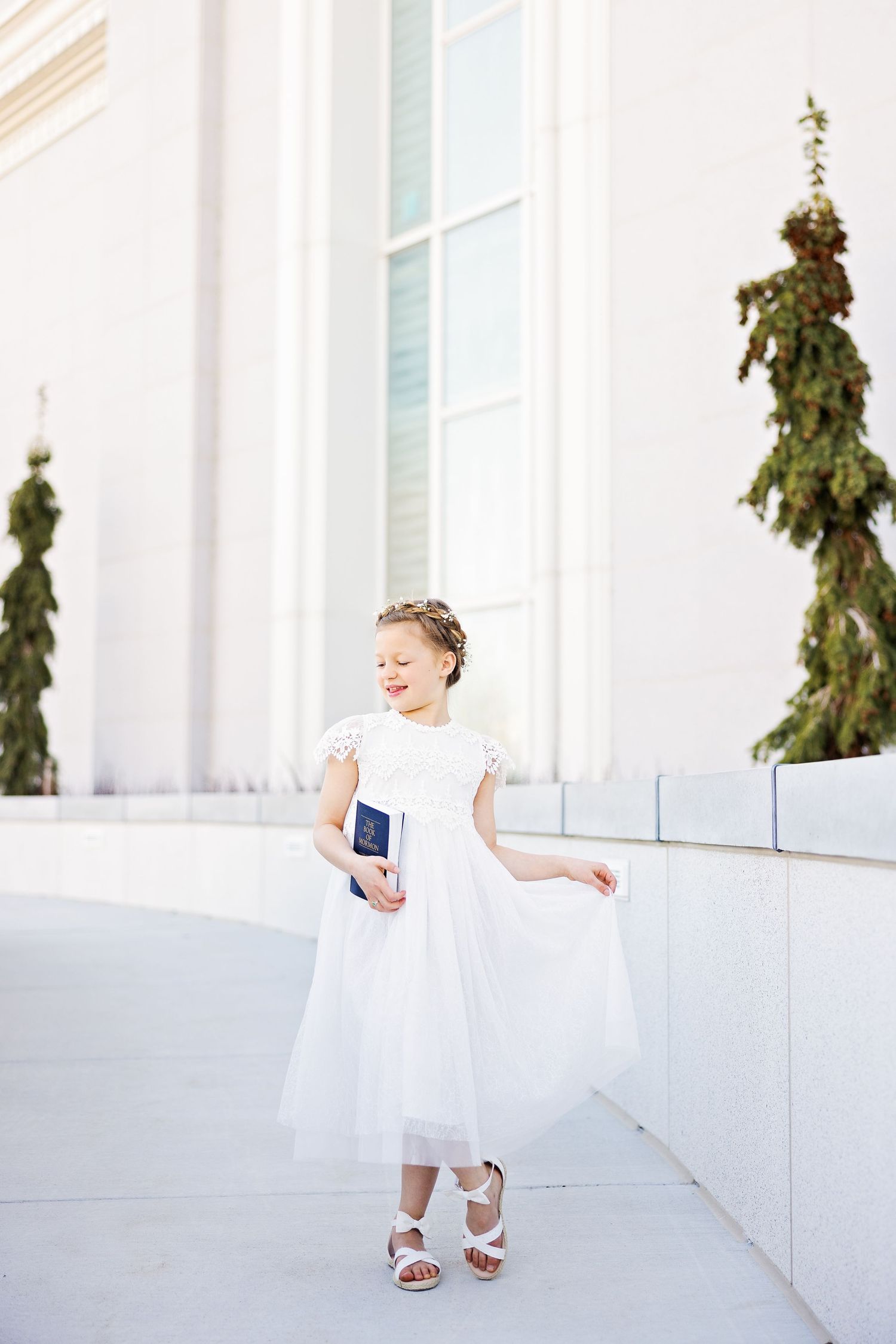 A person in a white dress twirls on a walkway near white columns and greenery.