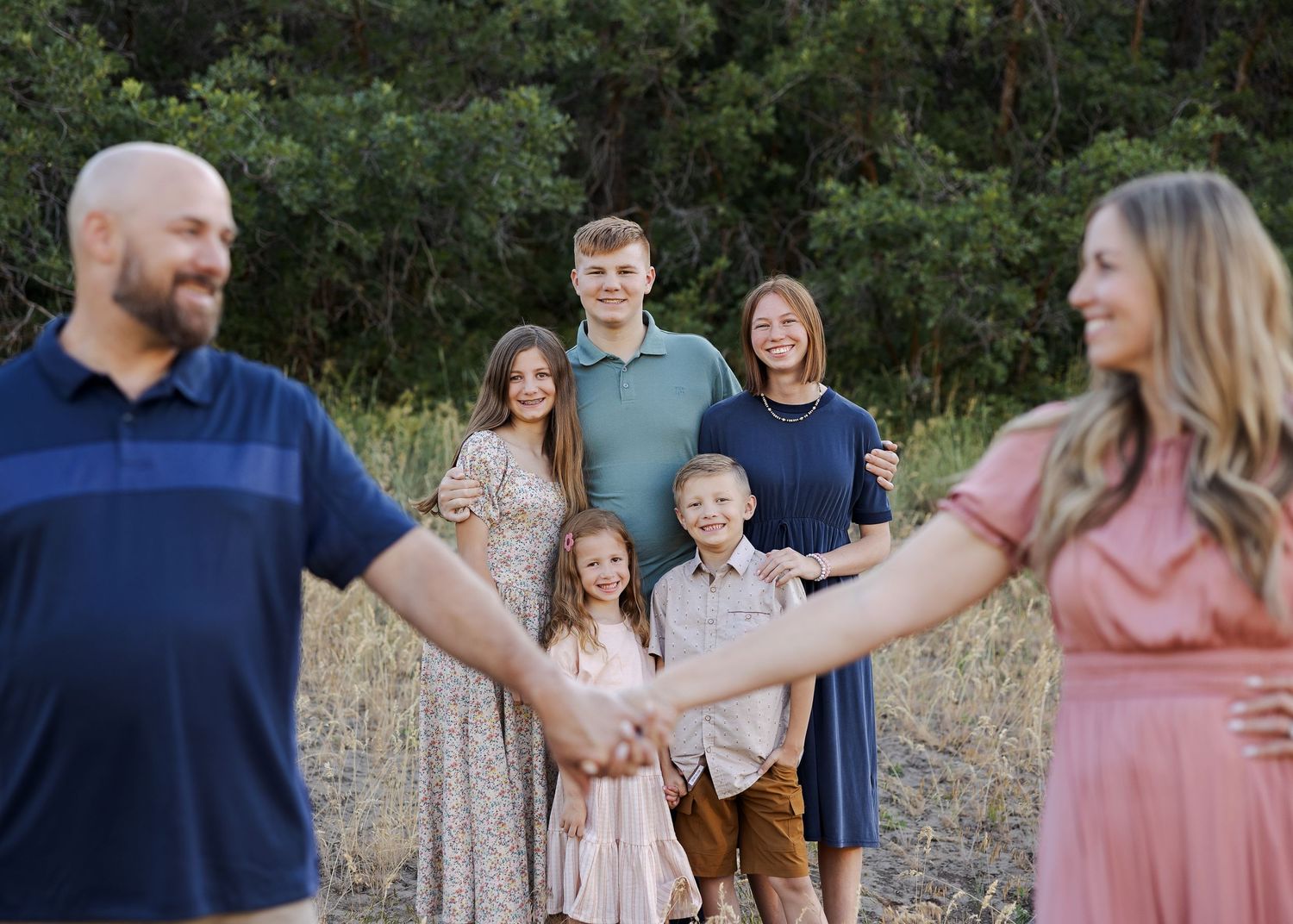 Group photo of family members holding hands in a circle against natural backdrop.