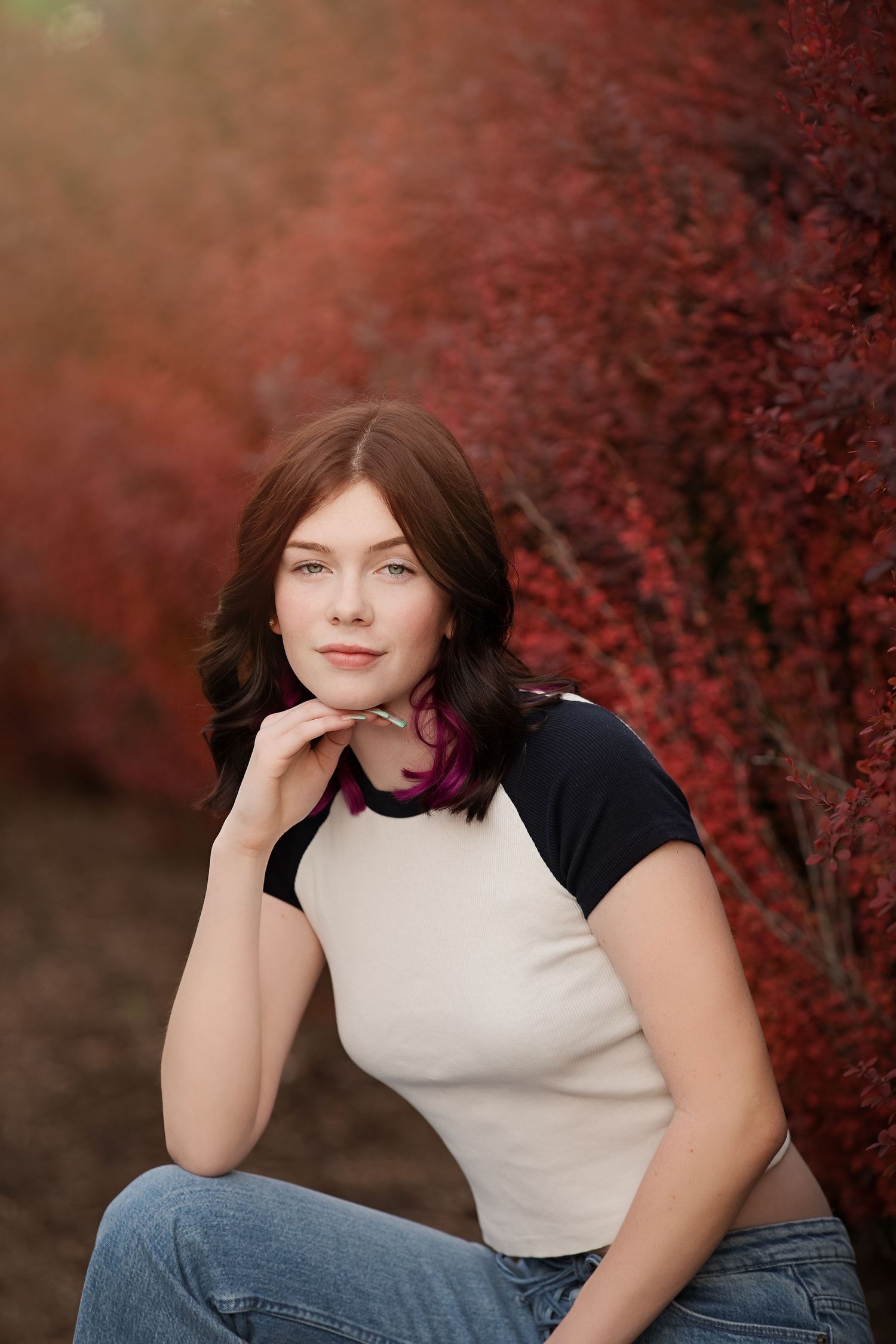 Portrait of someone posing outdoors against red autumn foliage wearing a baseball tee and purple scarf.