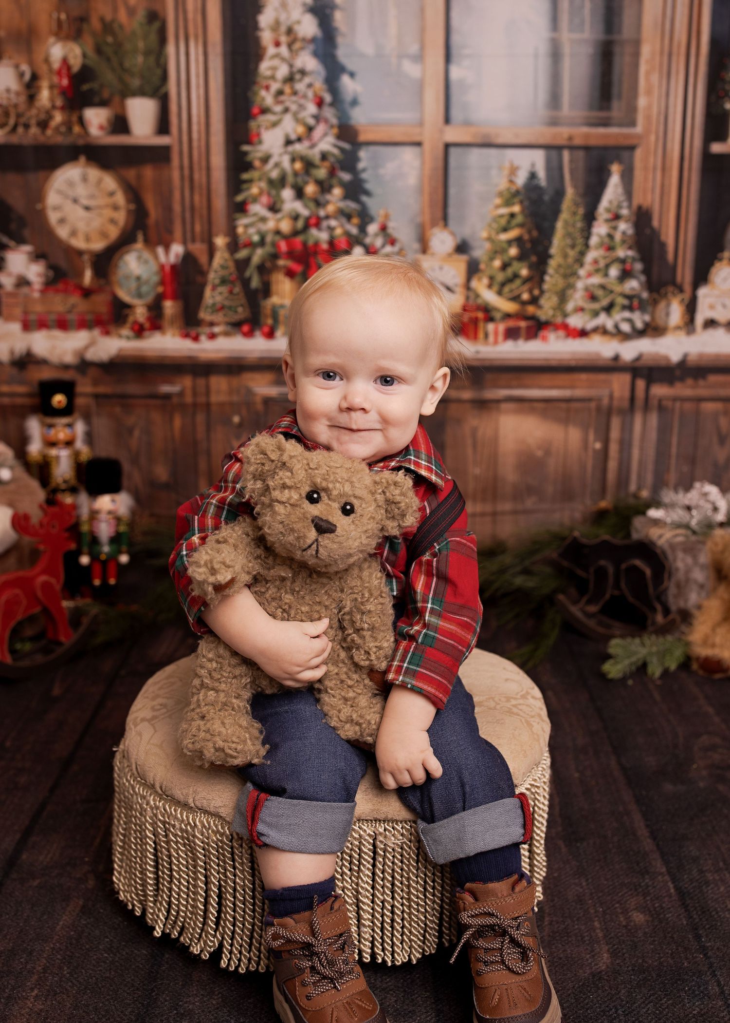 A small child sits on a fringed chair surrounded by Christmas decorations and holds a plush teddy bear.