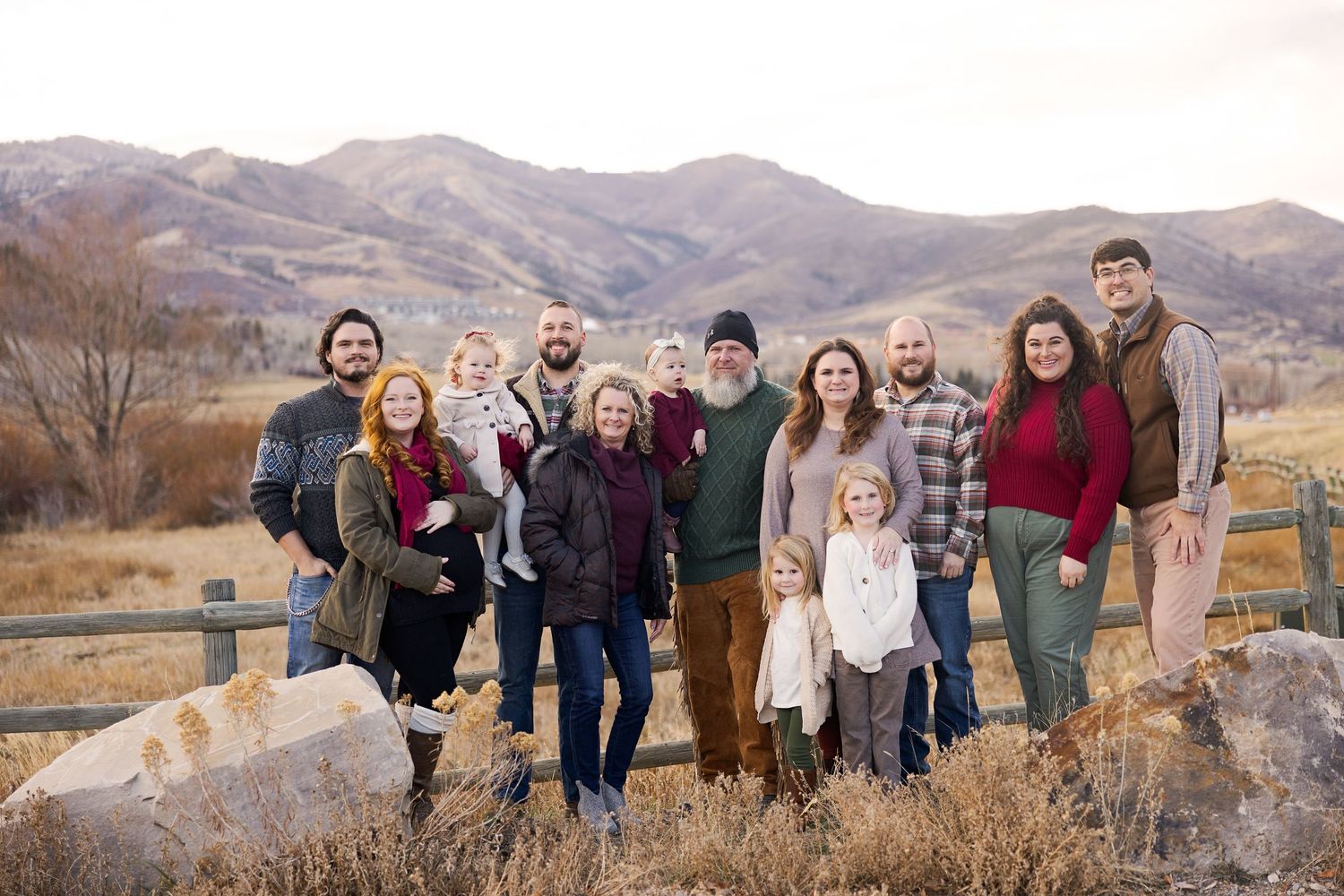 A group of people pose together on a rocky outcrop with mountains and autumn foliage in the background.