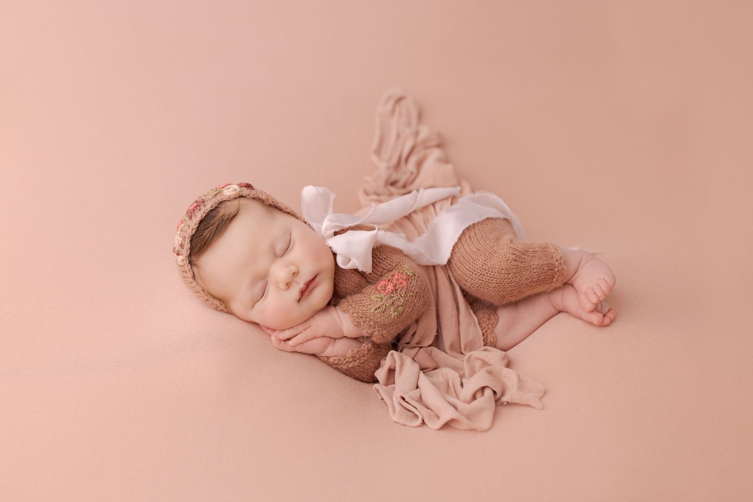 Sleeping newborn in pink outfit resting peacefully on soft pink backdrop.