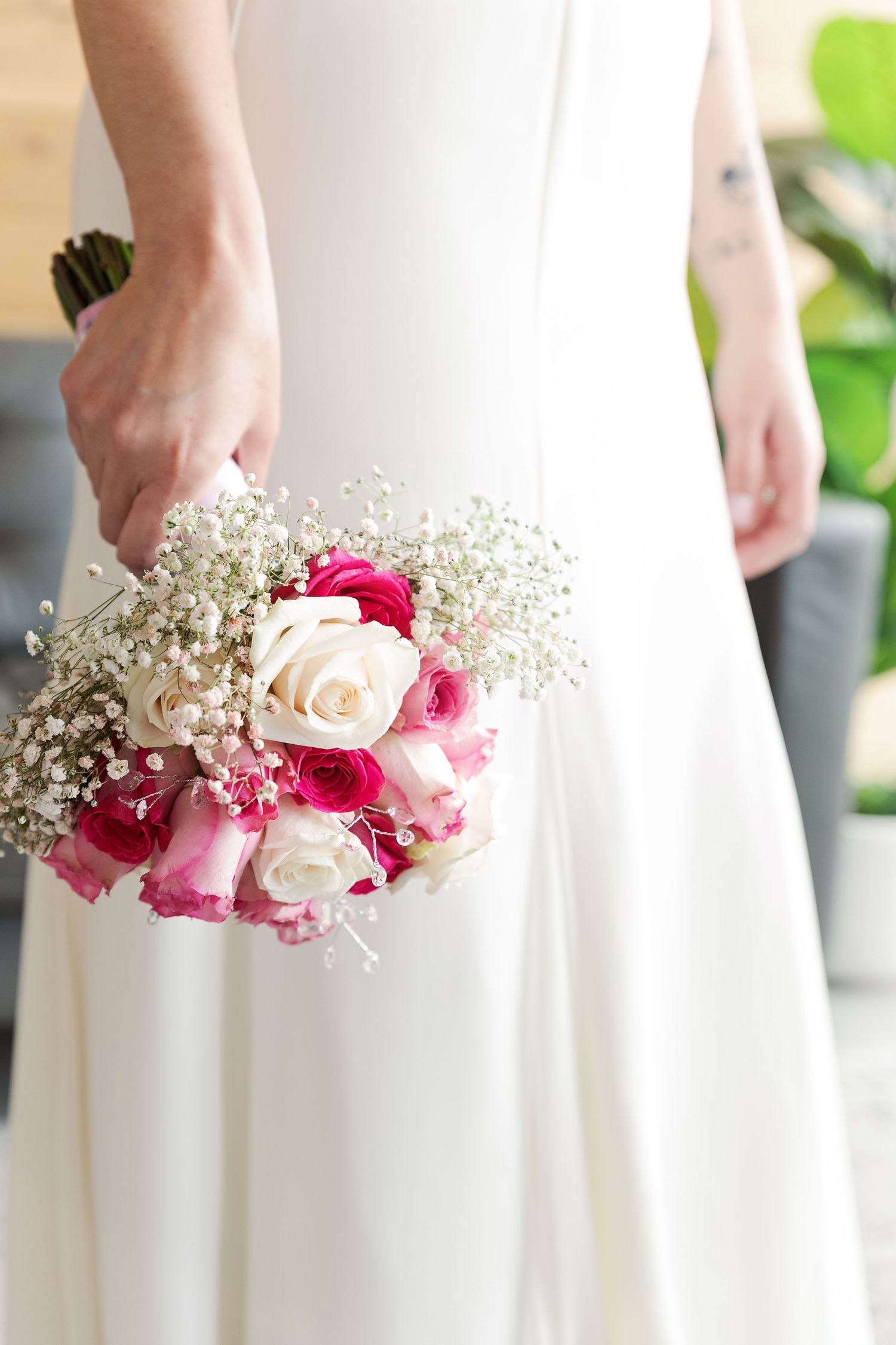 Elegant bridal bouquet with pink and white roses mixed with baby's breath against white dress.