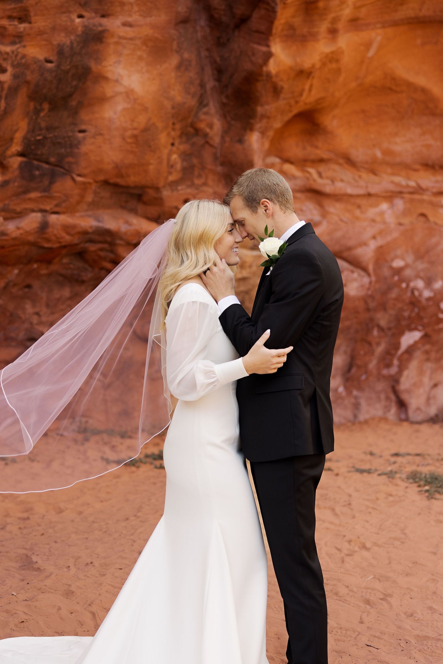 Tender moment between newlyweds against striking red rock formations.