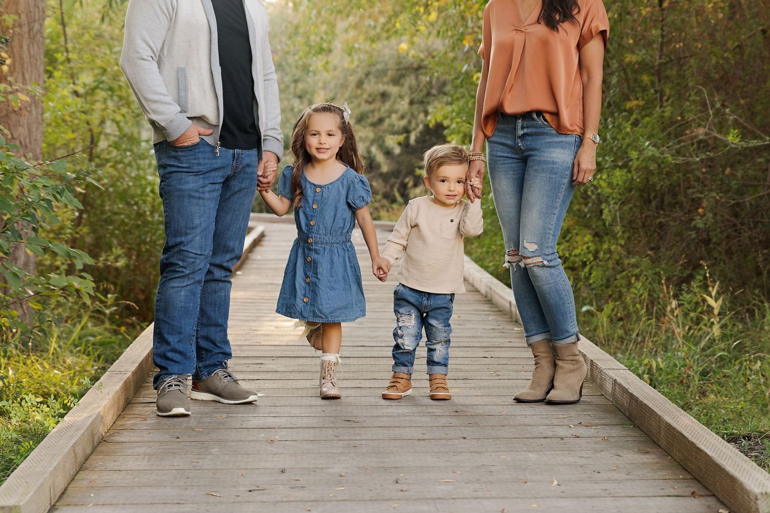 A family walks together holding hands on a wooden boardwalk path through nature.